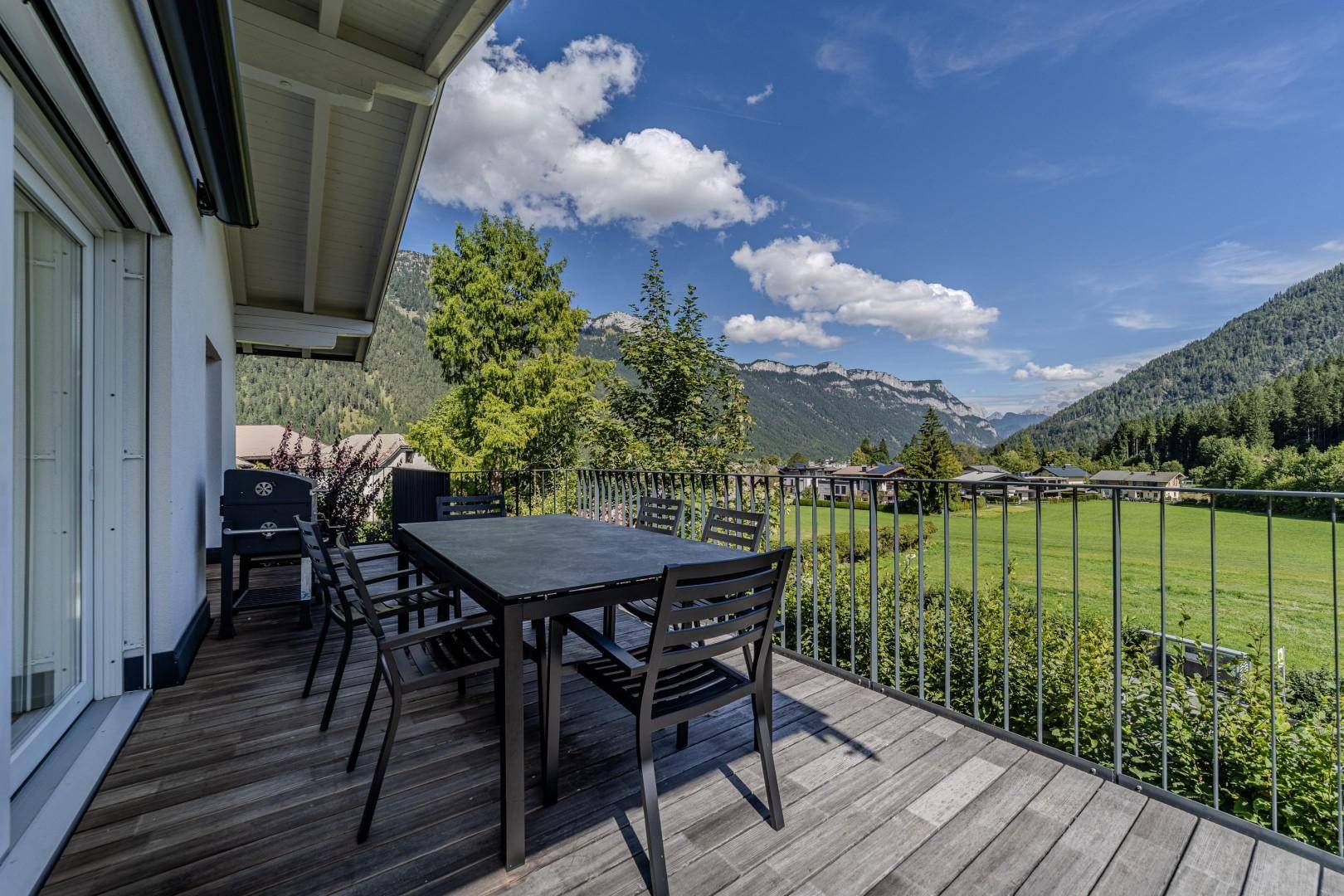 Geräumiger Balkon mit Esstisch und Stühlen, bietet einen weiten Blick auf die umliegende Berglandschaft und grüne Wiesen.