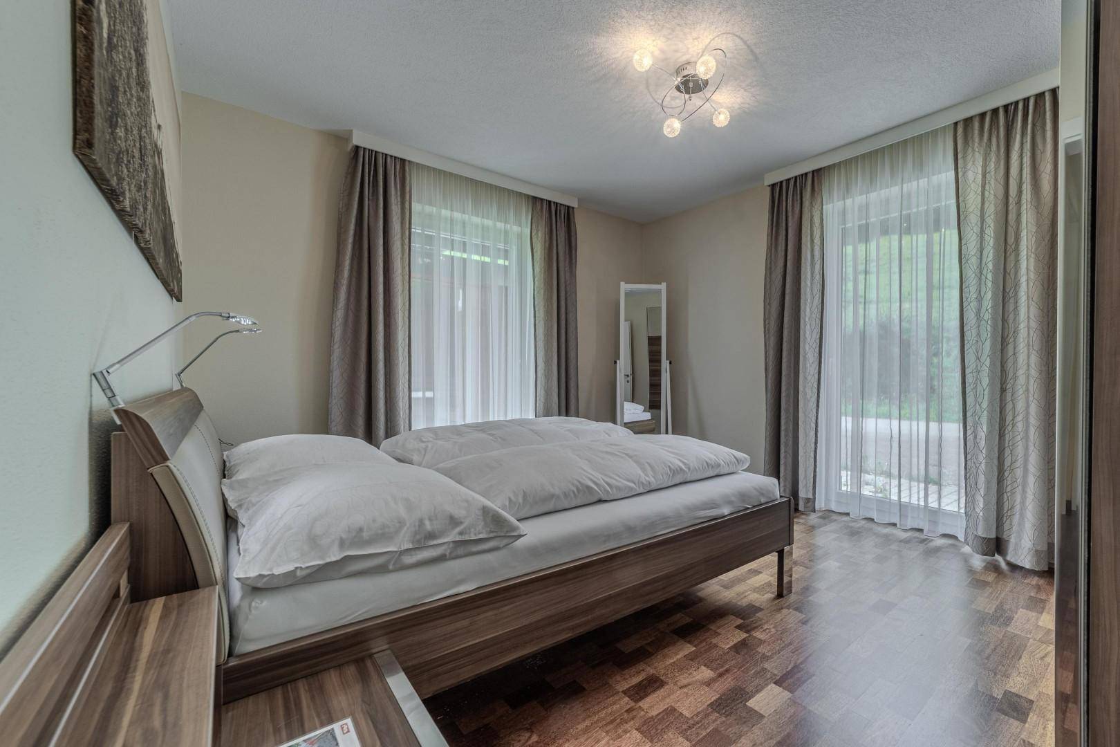 Helles Schlafzimmer mit Holzbett, Parkettboden und Zugang zu einer Terrasse oder Balkon.