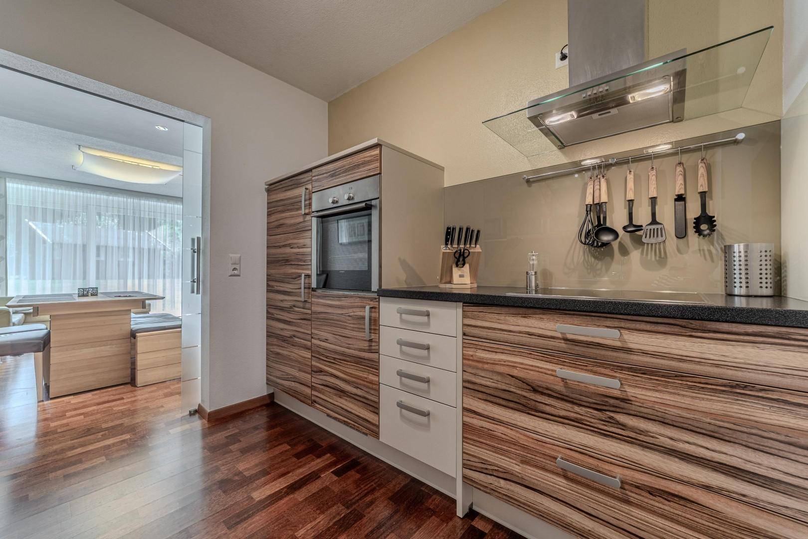 Moderne Küchenzeile mit Holzfronten, Einbaugeräten und Blick in den Essbereich.