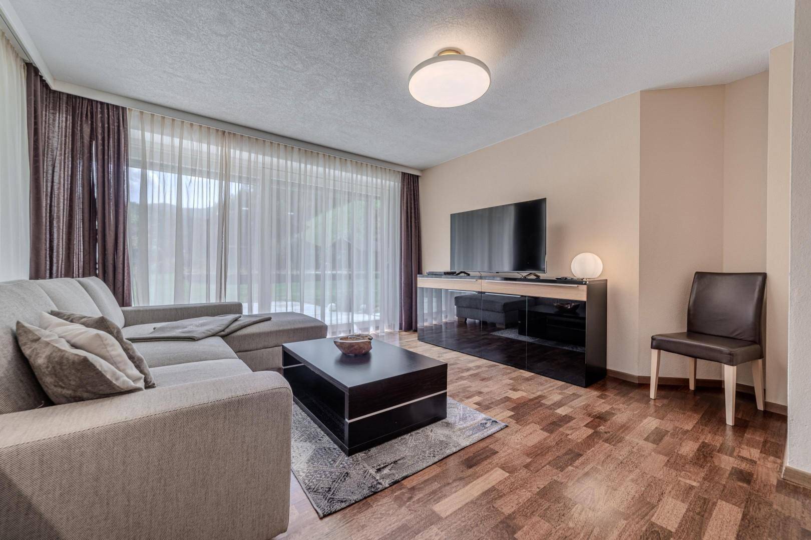 Heller Wohnbereich mit großem Flachbildfernseher, Sofa und Zugang zur Terrasse.