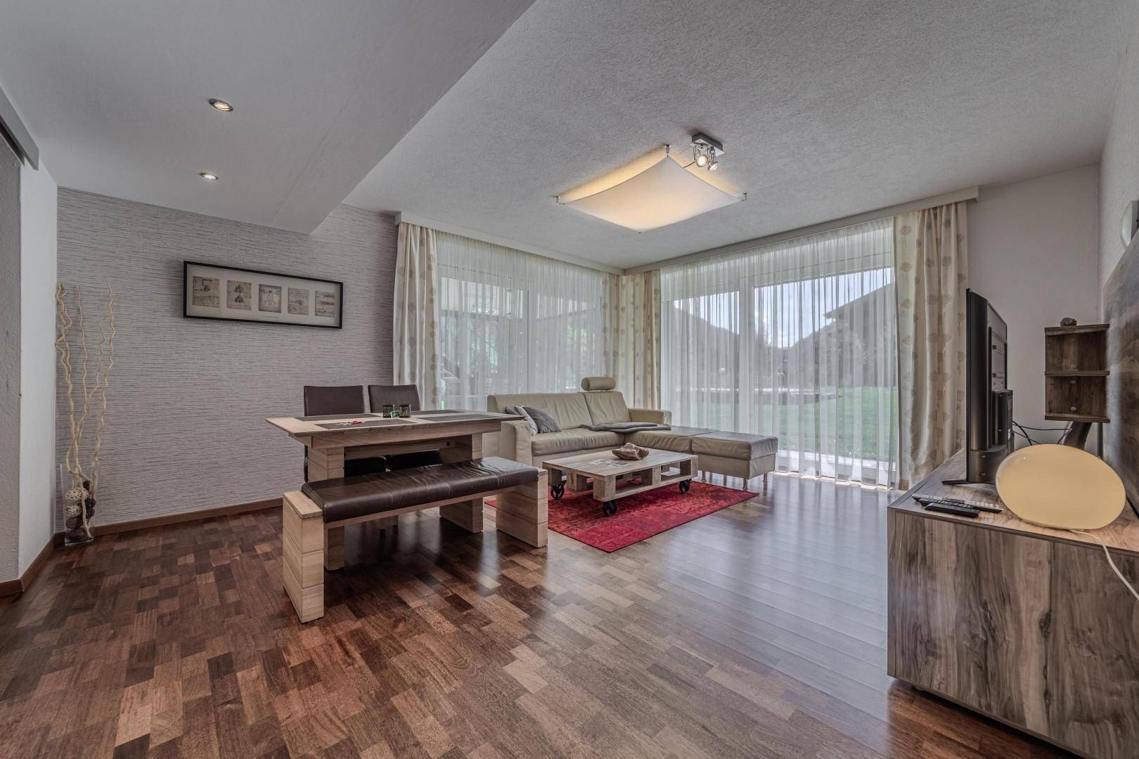 Offener Wohn- und Essbereich mit Holzboden, großem Sofa und Zugang zum Garten.