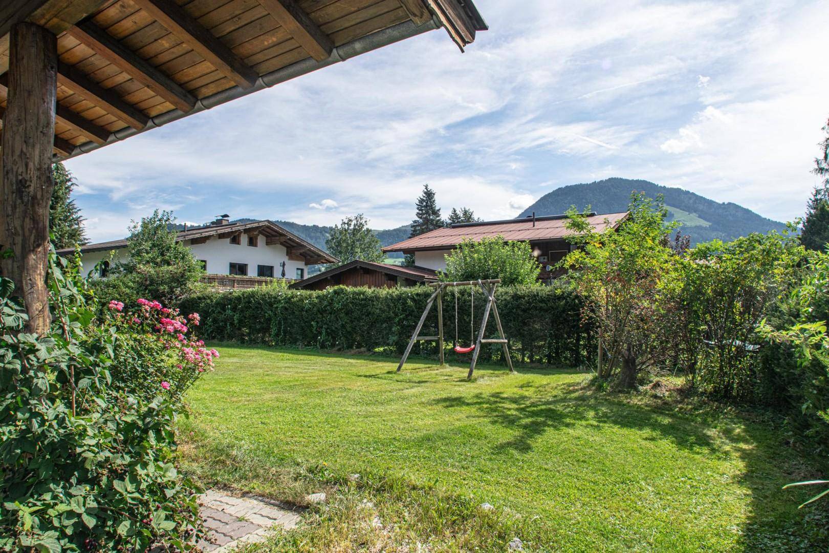 Weitläufiger Gartenbereich mit Schaukel und Hecke, umgeben von grüner Landschaft.