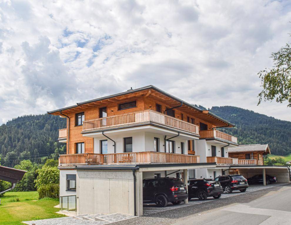 Modernes Apartmentgebäude mit Carports und Balkonen, eingebettet in eine grüne Berglandschaft.
