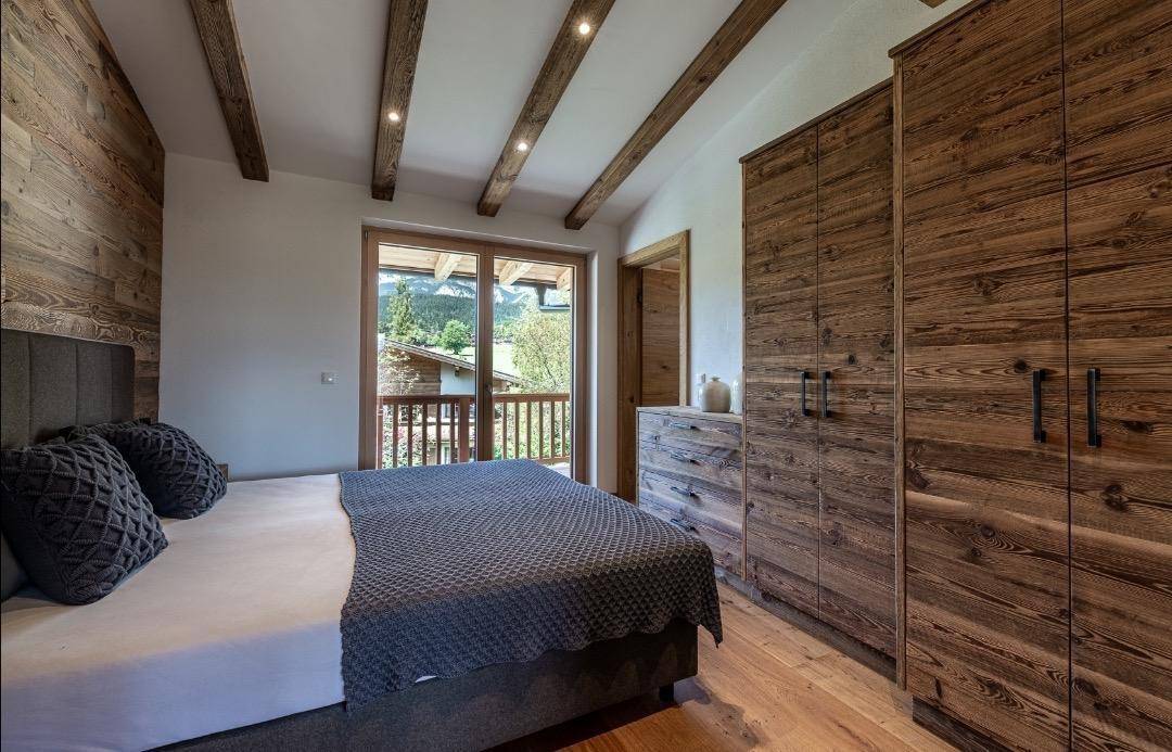 Helles Schlafzimmer mit Holzkleiderschrank, Doppelbett und Zugang zu einem Balkon mit Aussicht.