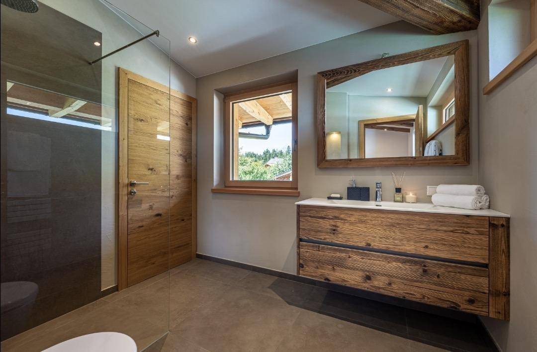 Geräumiges Badezimmer mit Holzwaschtisch, großem Spiegel und Fenster für natürliches Licht.