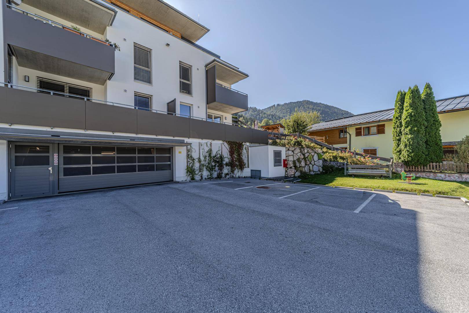 Moderne Wohnanlage mit Tiefgaragenzufahrt und Außenstellplätzen in grüner Umgebung.