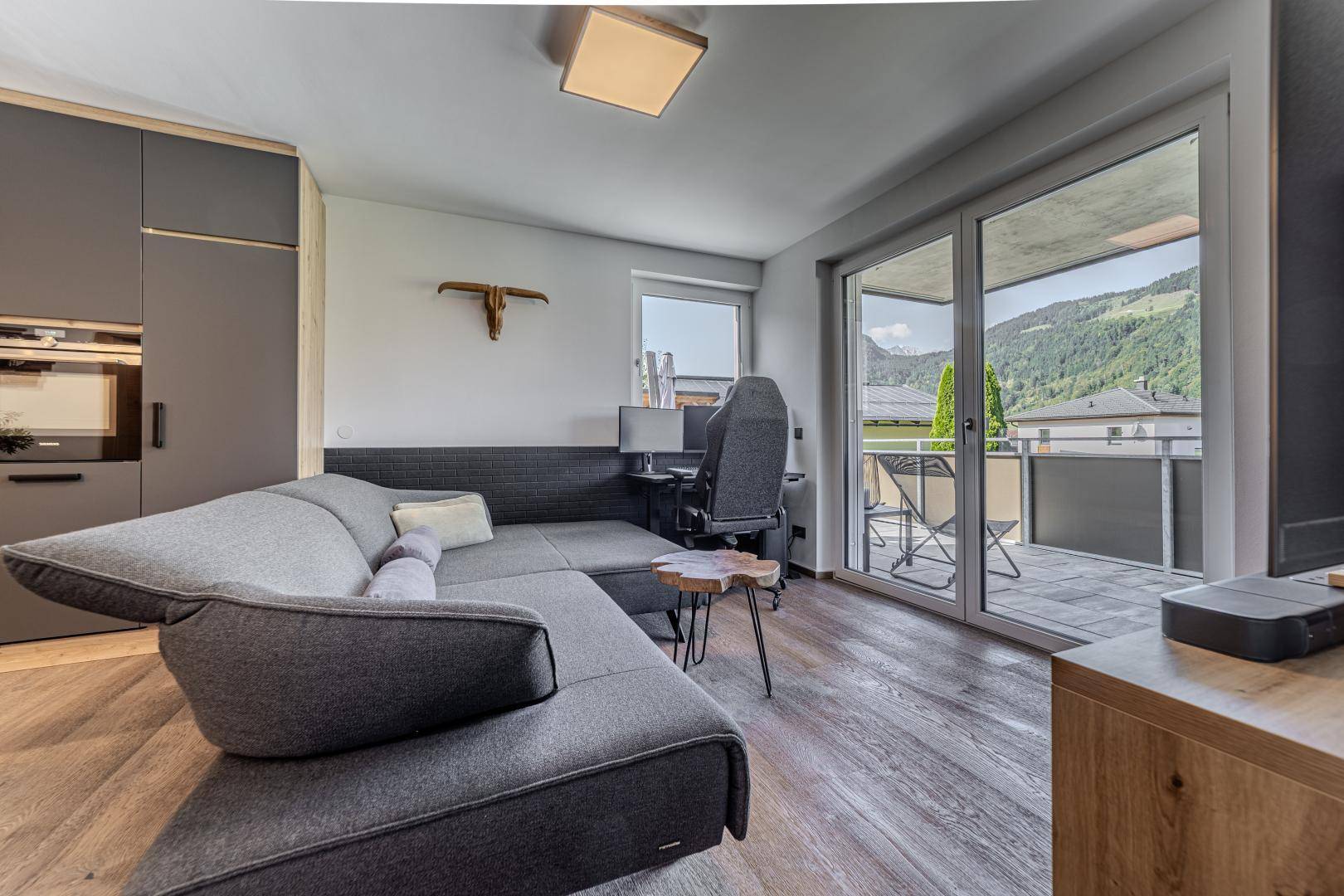 Helles Wohnzimmer mit Zugang zum Balkon und Bergblick, ausgestattet mit einem Arbeitsbereich.