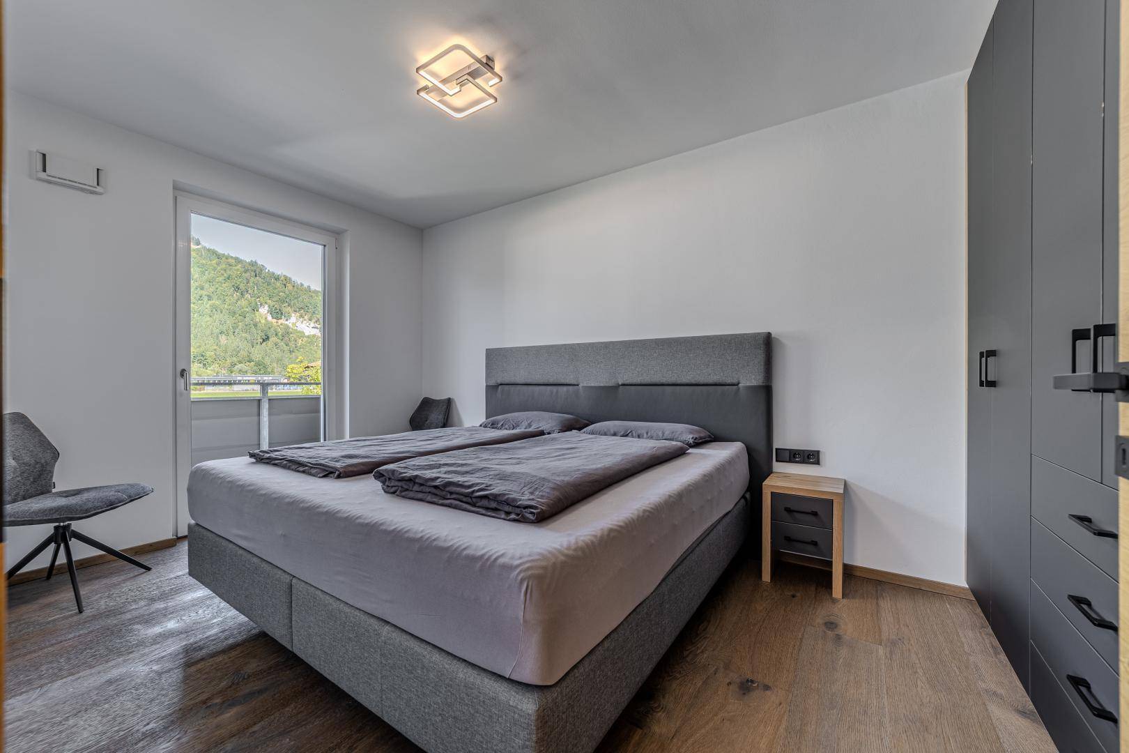 Modernes Schlafzimmer mit Doppelbett, Holzboden und direktem Zugang zum sonnigen Balkon.