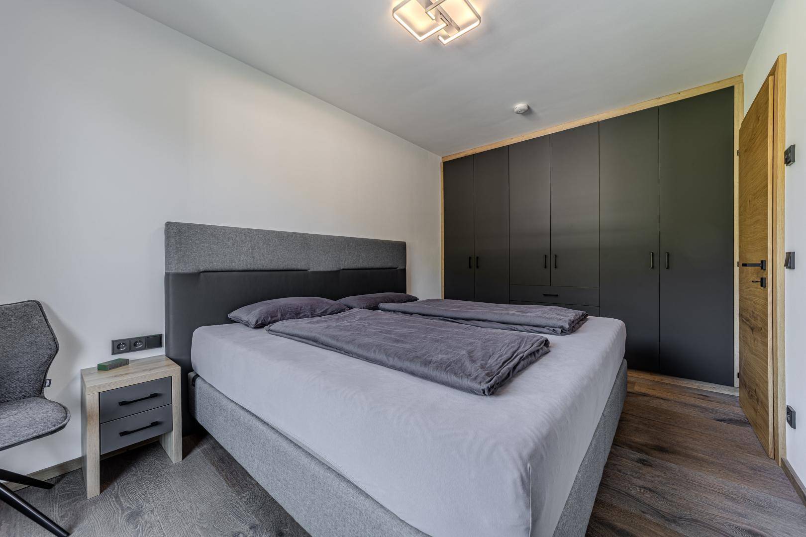 Schlafzimmer mit großem Doppelbett und eleganten, maßgefertigten Einbauschränken in dunklem Design.