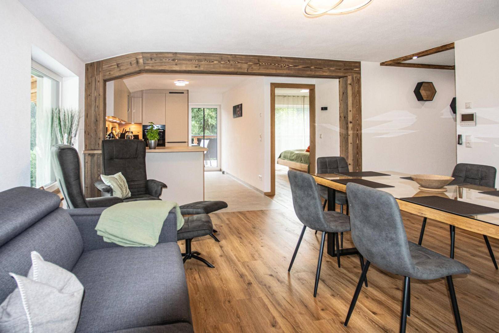 Gemütlicher Wohn- und Essbereich mit Holzboden, offener Küche und Zugang zu einem weiteren Zimmer.