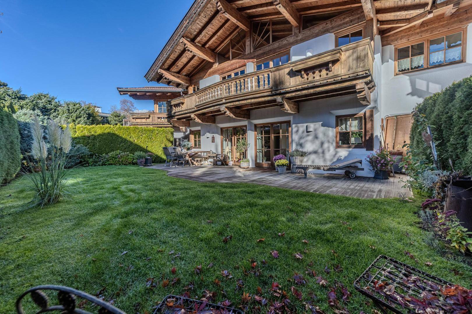 Weitläufiger Garten mit Holzterrasse und Grillbereich vor einem traditionellen Haus im Alpenstil.