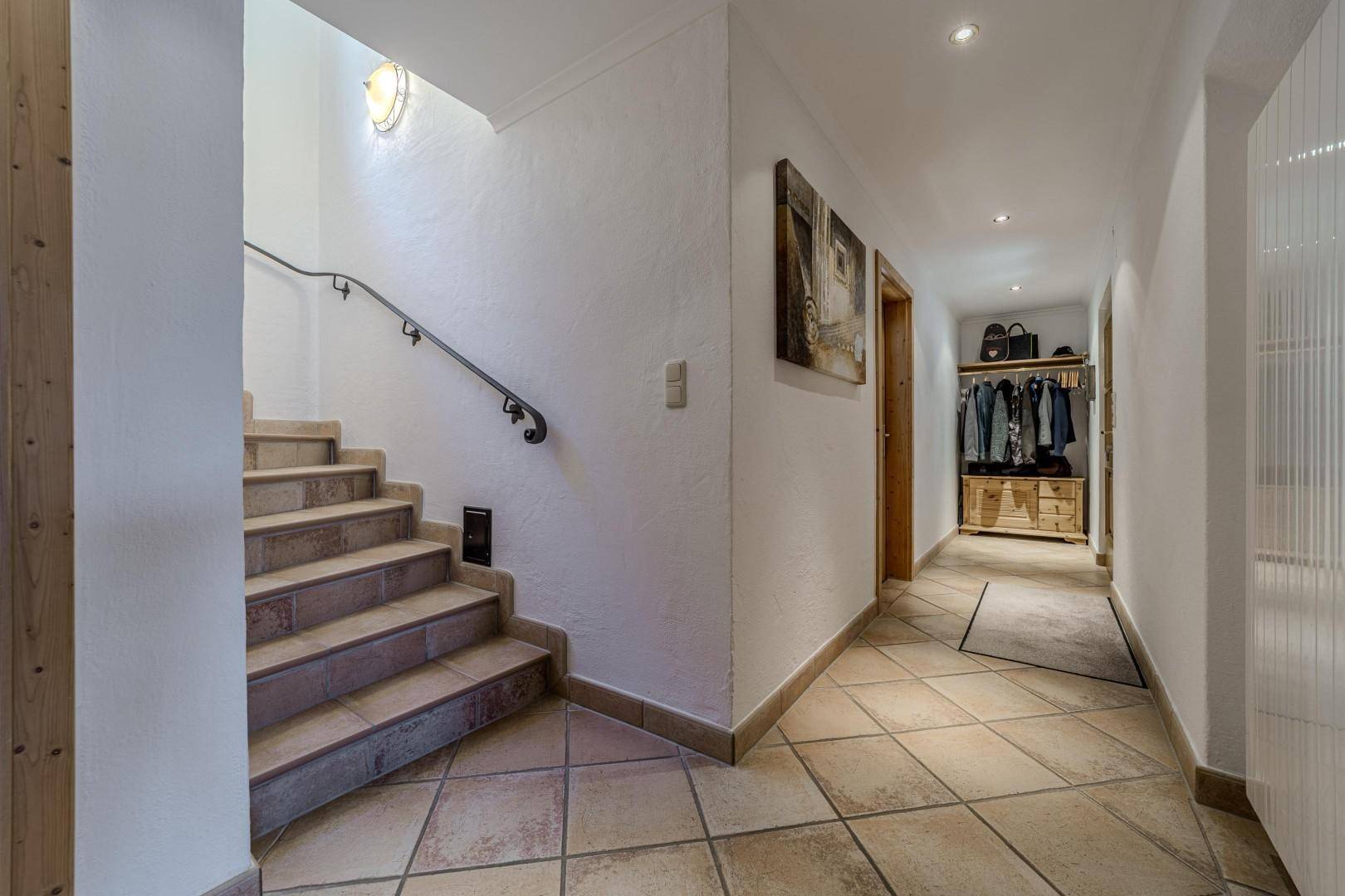 Eingangsbereich mit gefliestem Boden, Holztreppe und Garderobe.