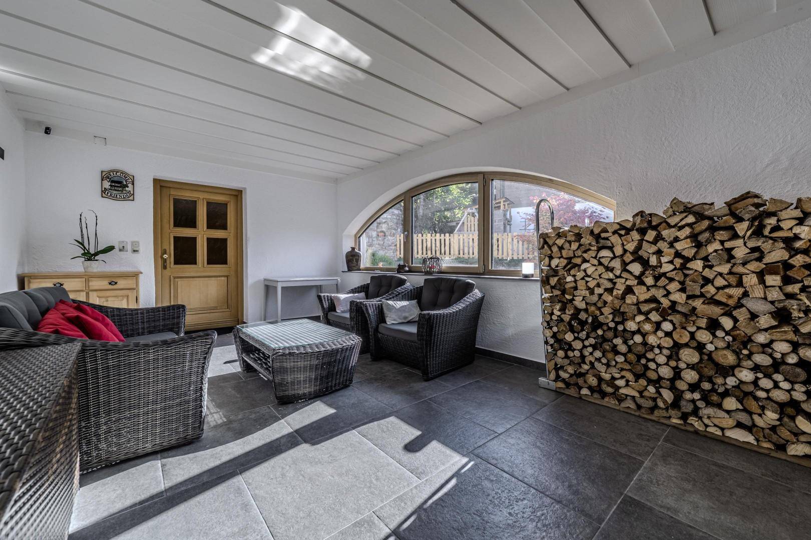 Gemütlicher Wintergarten mit Holzstapel, Korbmöbeln und traditioneller Holztür.