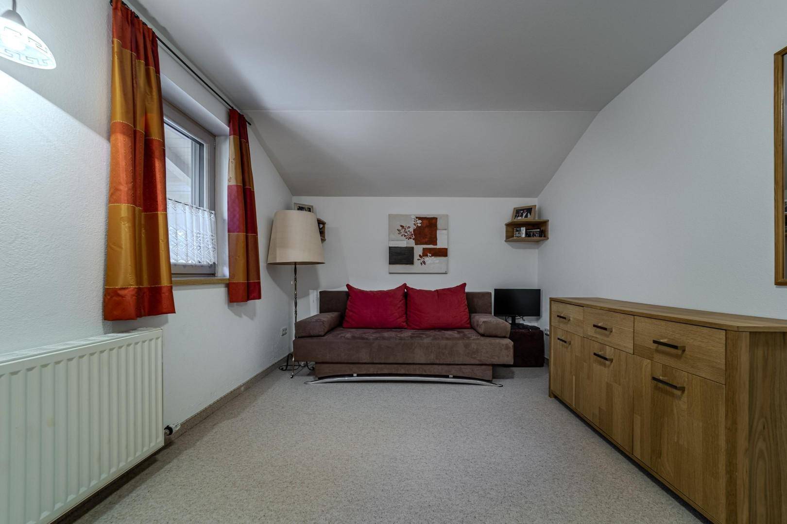 Helles Zimmer mit Sofa, Teppichboden und Holzkommode.