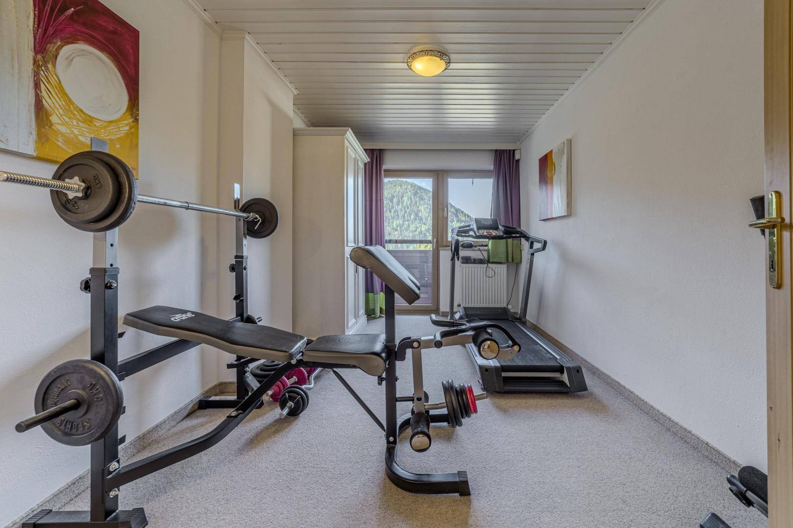 Fitnessraum mit Hantelbank, Laufband und Zugang zum Balkon mit Bergblick.