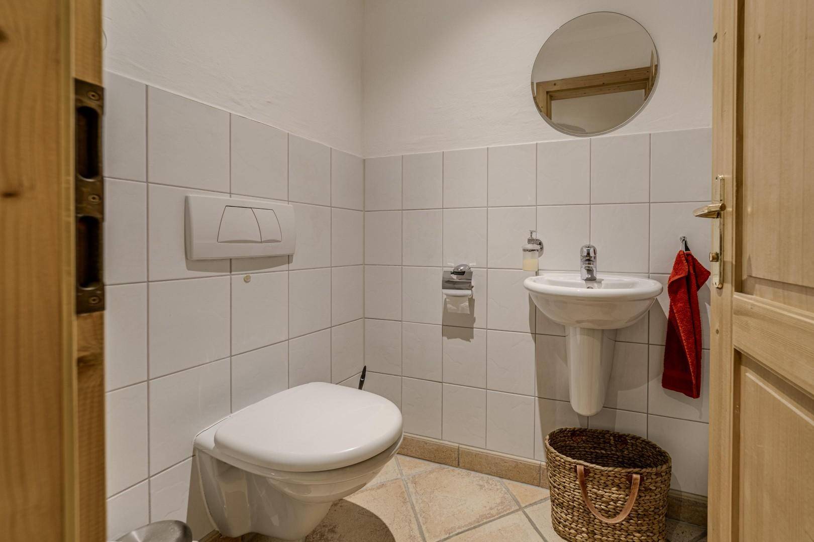 Kleines Gäste-WC mit wandhängender Toilette, Waschbecken und rundem Spiegel.