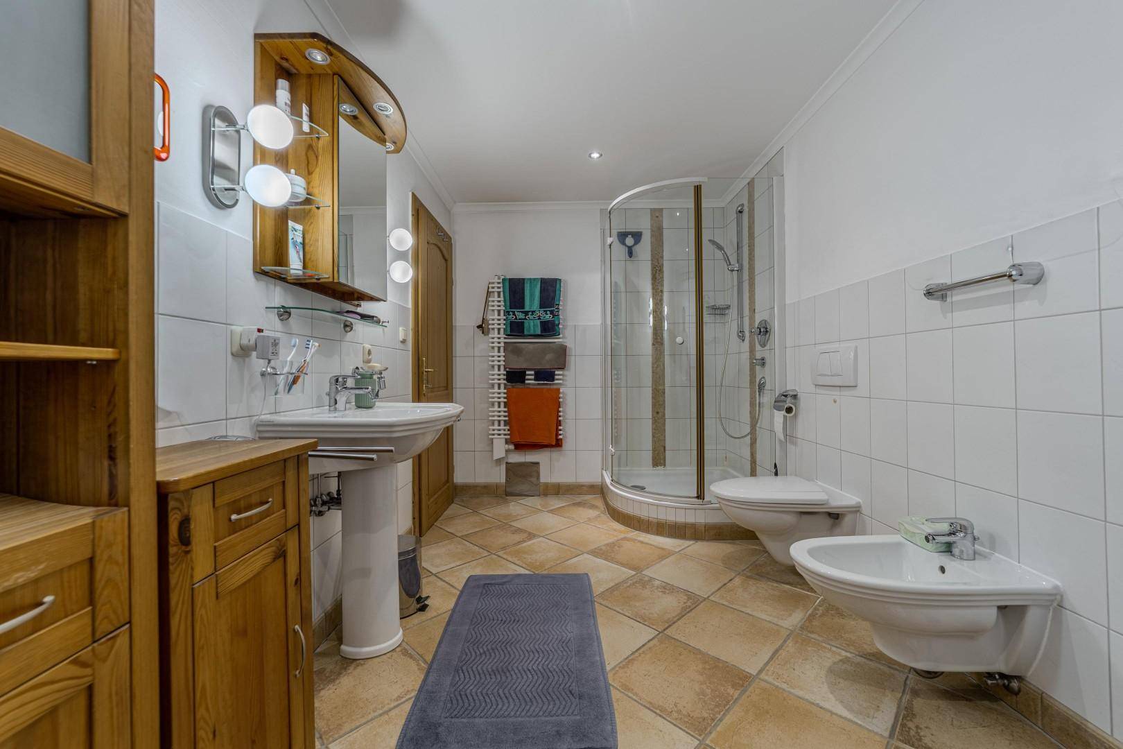 Geräumiges Badezimmer mit Dusche, Bidet, Waschtisch und Holzmöbeln.