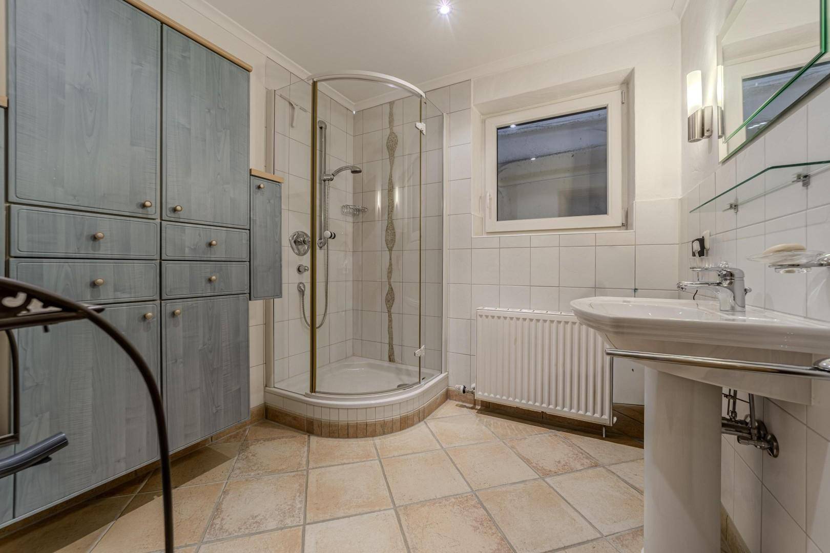 Funktionales Badezimmer mit Duschkabine, Waschbecken, Fenster und praktischen Schränken.