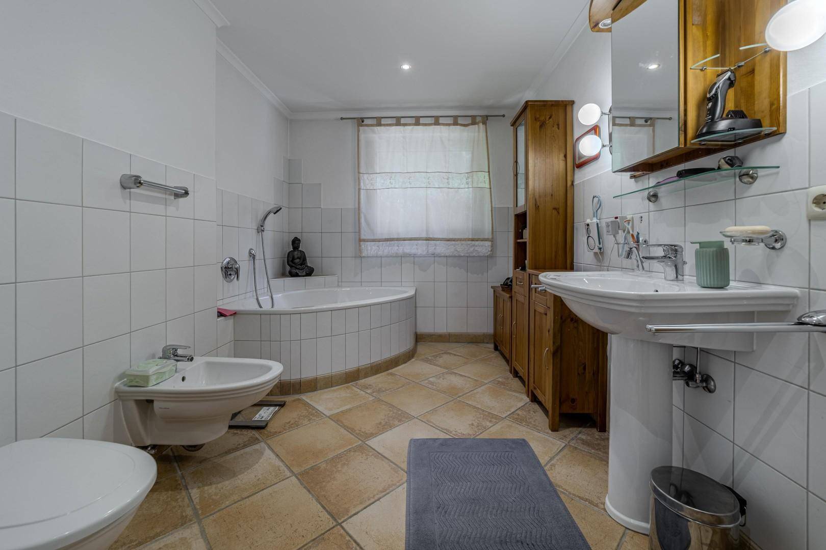 Helles Badezimmer mit Badewanne, Bidet, Waschtisch und Holzschrank.