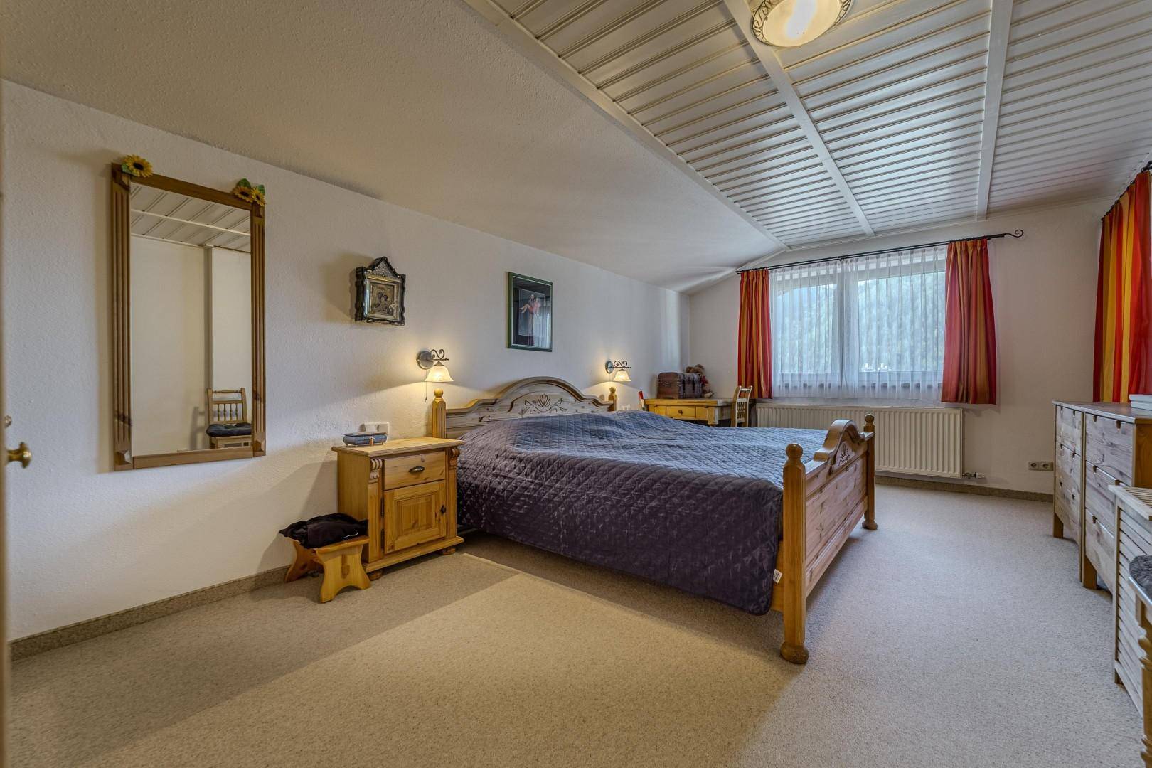 Helles Schlafzimmer mit Holzbett, Nachttischen und Fenster mit Vorhängen.