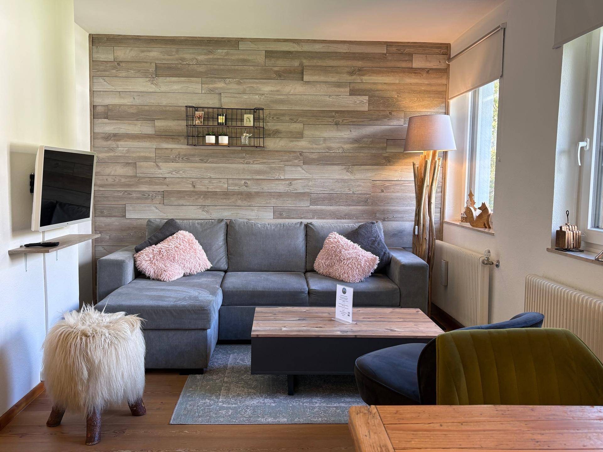 Gemütliches Wohnzimmer mit grauem Ecksofa, Holzwandverkleidung und modernem Flachbildfernseher.