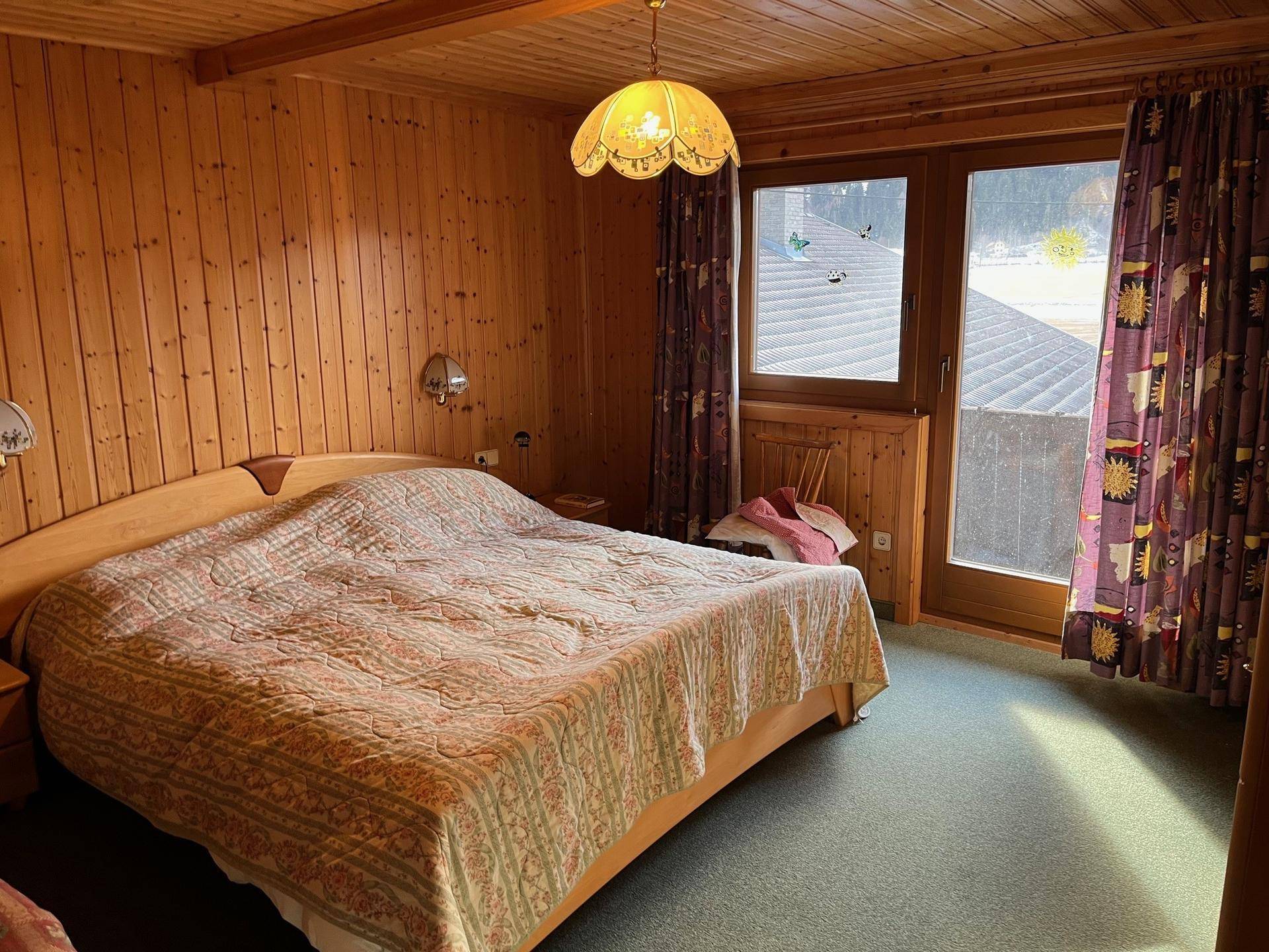 Gemütliches Schlafzimmer im Landhausstil mit viel Holz, Teppichboden und Zugang zum Balkon.