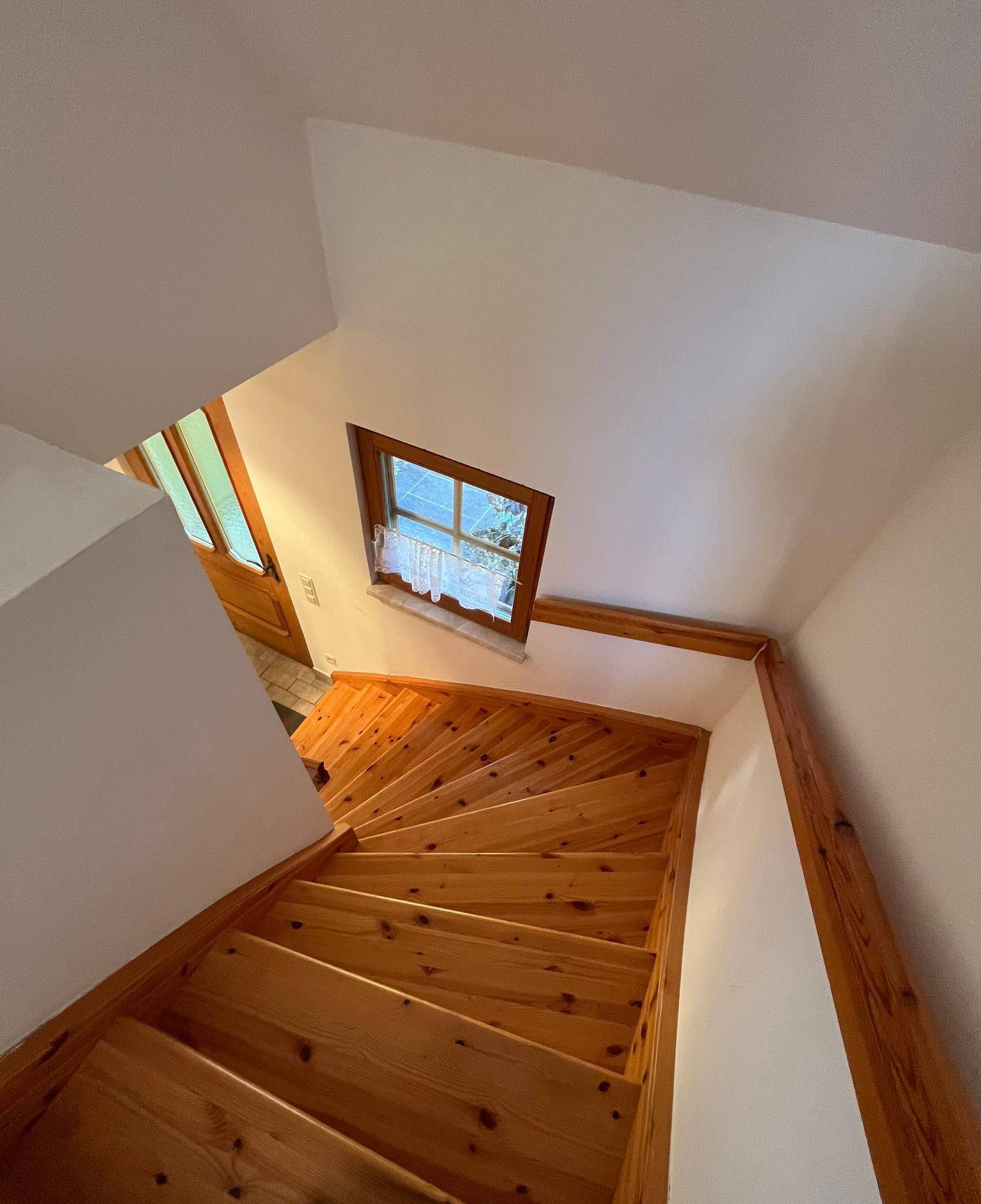 Holztreppe führt in das obere Stockwerk, beleuchtet durch ein Fenster.