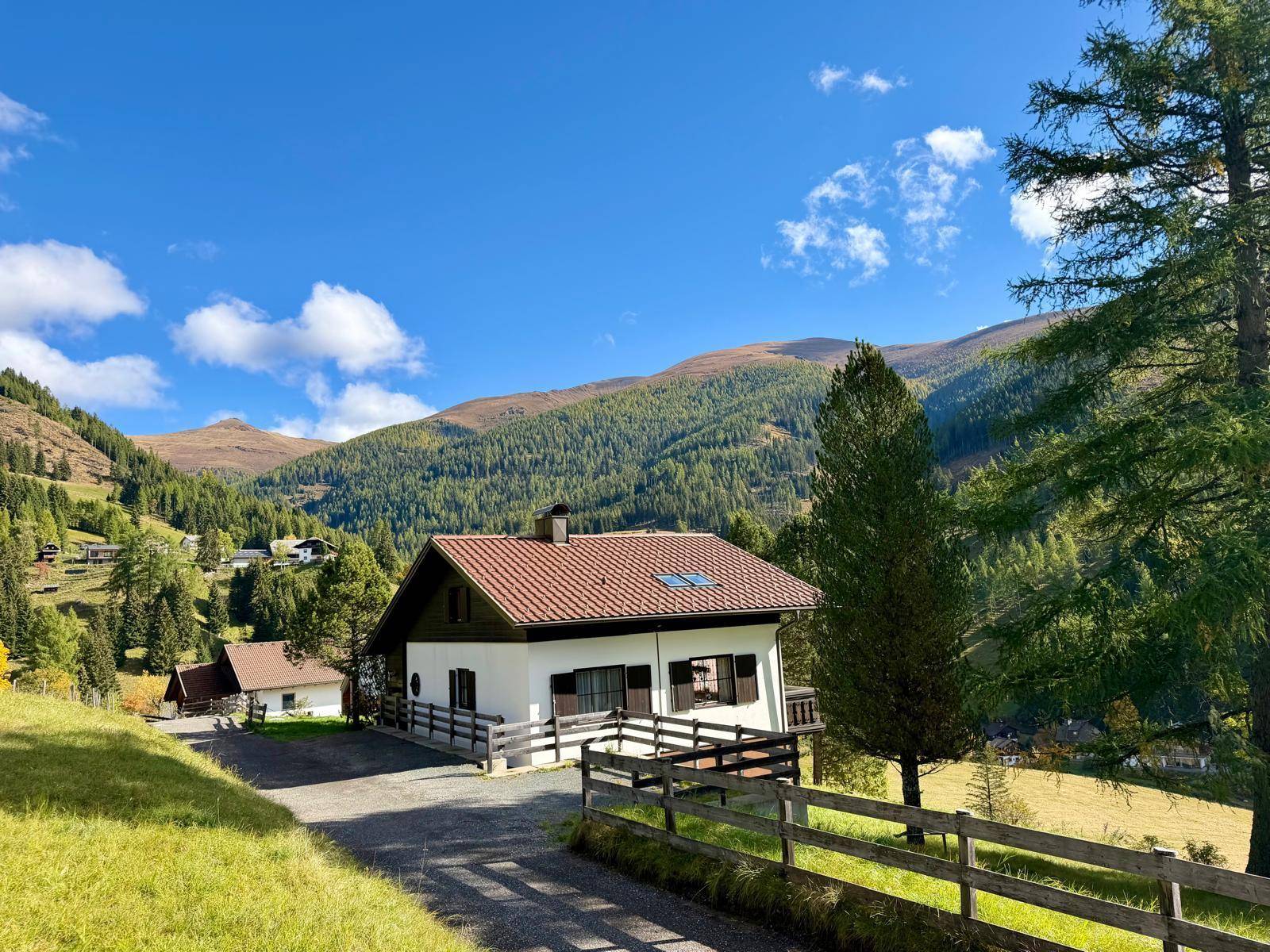 Freistehendes Haus mit rotem Ziegeldach und grünen Fensterläden in einer malerischen Berglandschaft.
