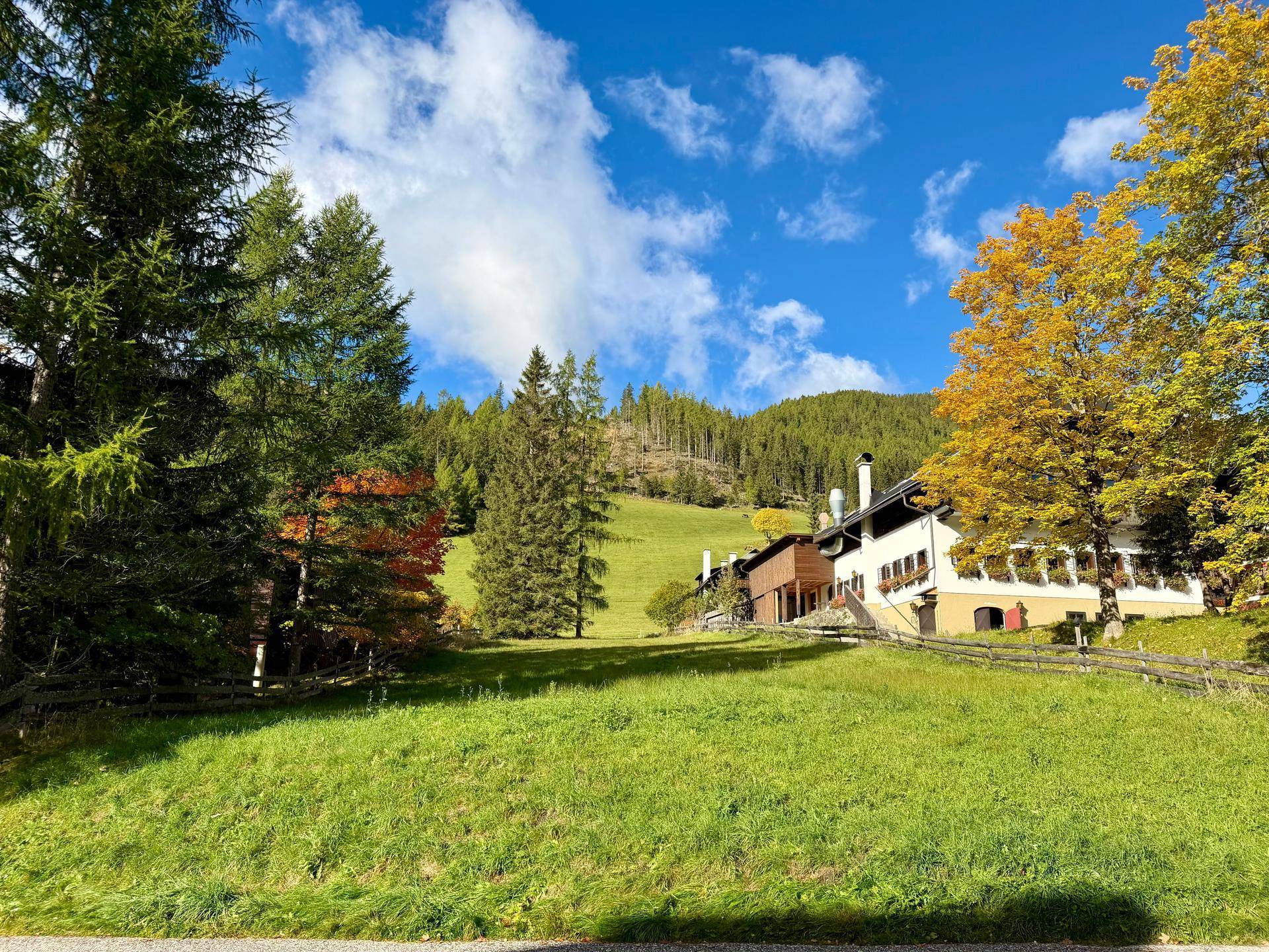 Traditionelles Gebäude eingebettet in eine idyllische Landschaft mit grünen Wiesen und hohen Bäumen.