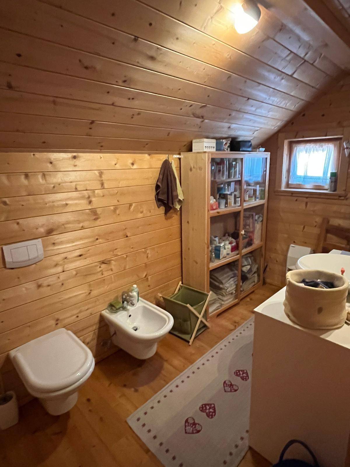 Rustikales Badezimmer mit Holzvertäfelung, WC, Bidet und Fenster für Tageslicht.