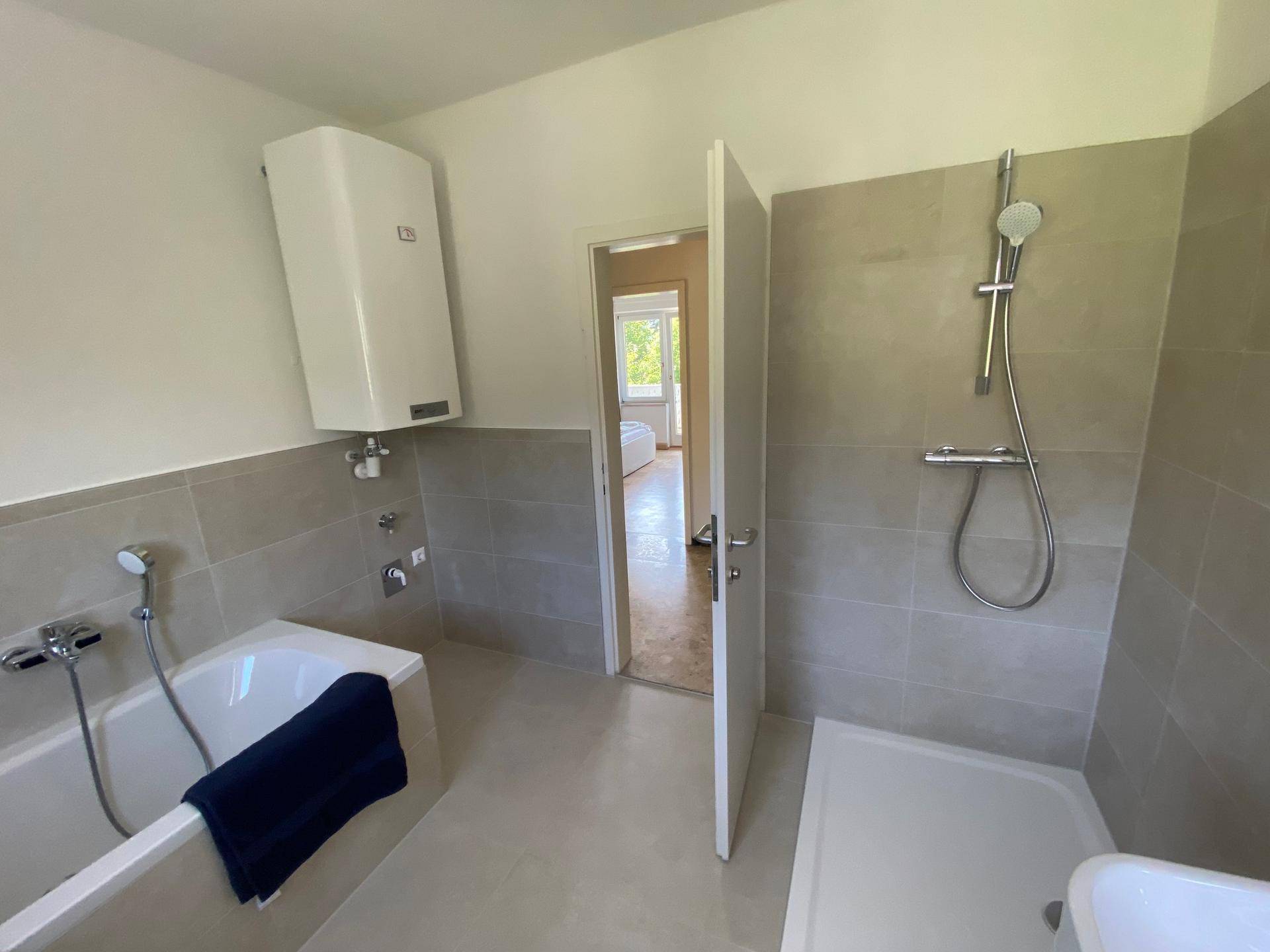 Helles Badezimmer mit Badewanne, Duschbereich und modernem Design, das zum Schlafzimmer führt.