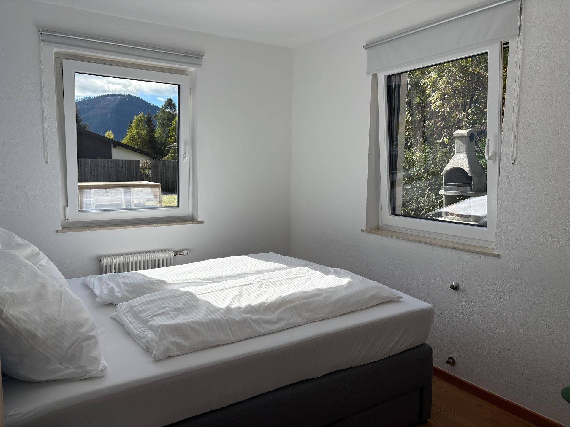 Schlafzimmer mit Doppelbett und Fenstern, die einen Blick auf den Außenbereich und Grillplatz bieten.