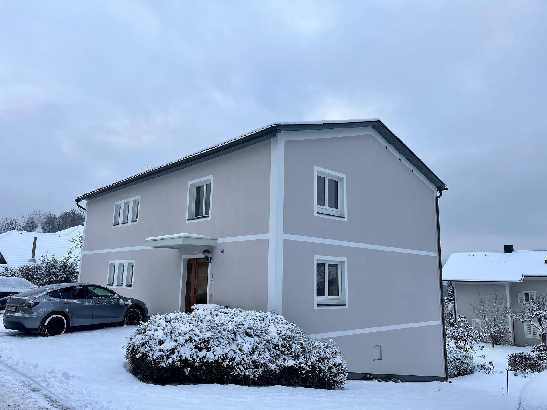 Modernes Einfamilienhaus mit heller Fassade und Satteldach, umgeben von Schnee im Winter.