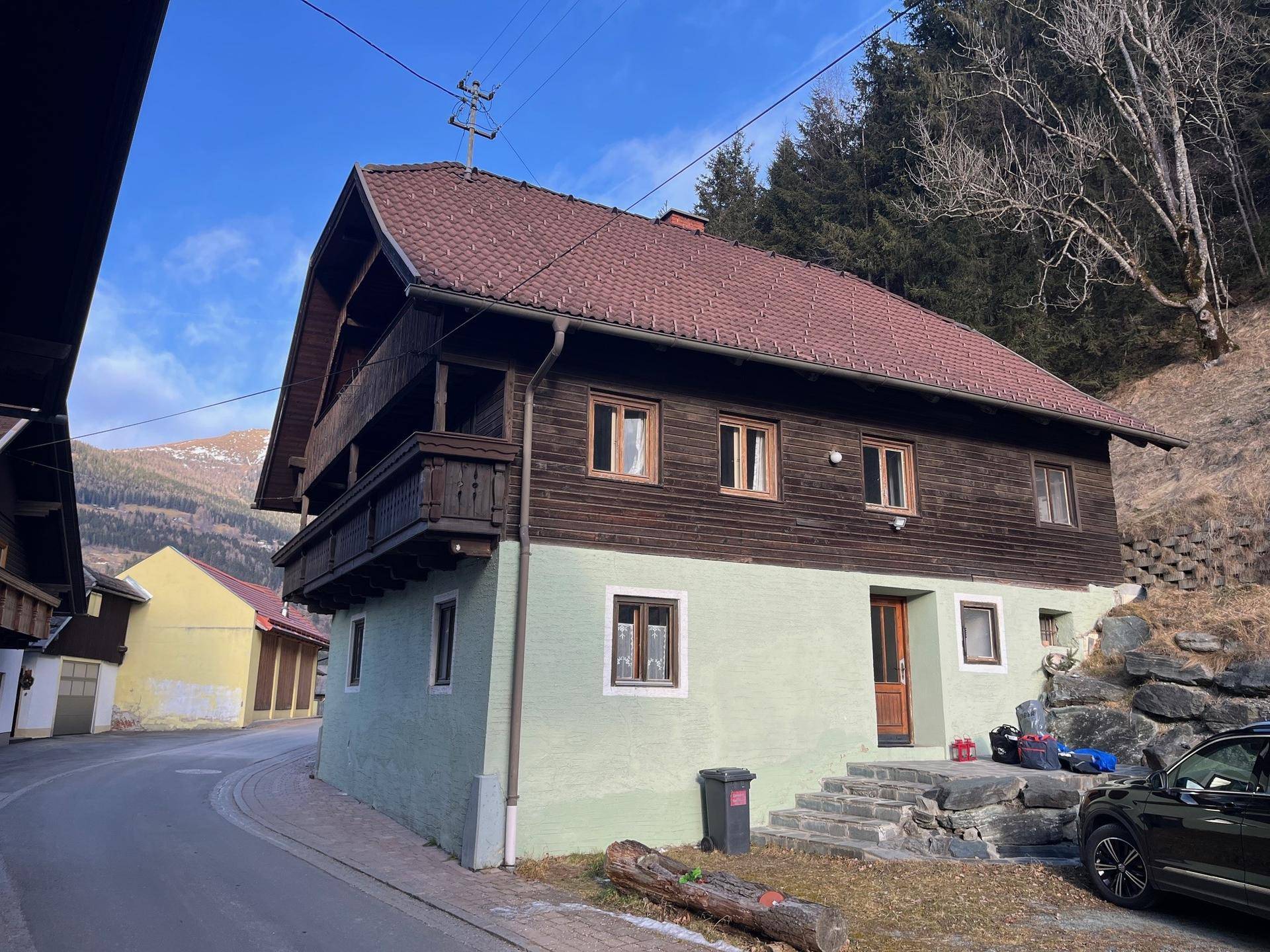 Charmantes alpines Haus mit Holzbalkonen und grüner Fassade, eingebettet in eine ländliche Umgebung.