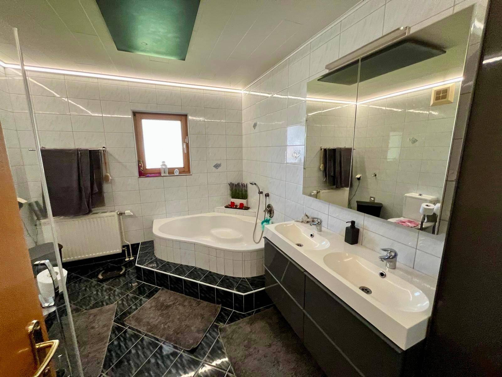 Modernes Badezimmer mit Eckbadewanne, Doppelwaschbecken und schwarz-weißen Fliesen.