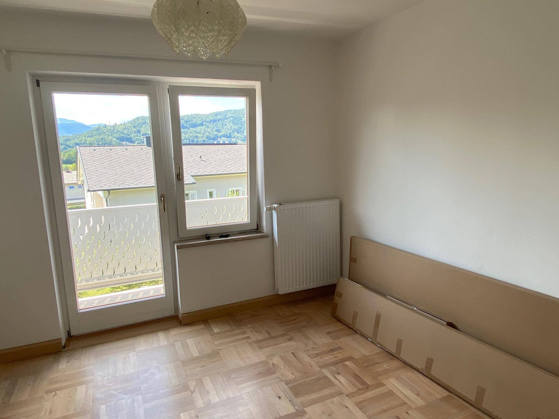 Schlafzimmer mit Parkettboden, großem Fenster und Balkonzugang, bereit zur Einrichtung.