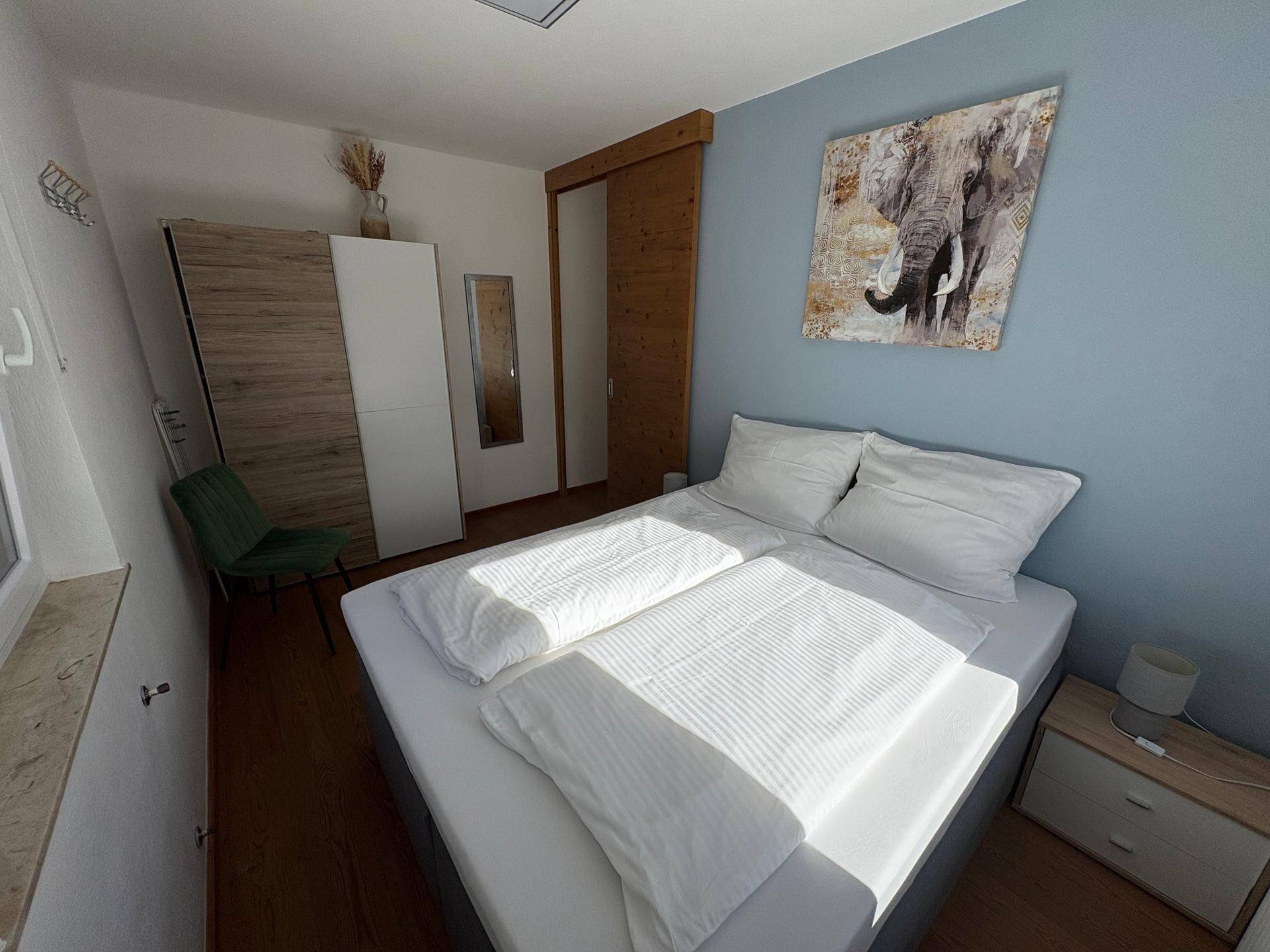 Modernes Schlafzimmer mit Doppelbett, Holzschrank und einer blauen Akzentwand für eine frische Atmosphäre.