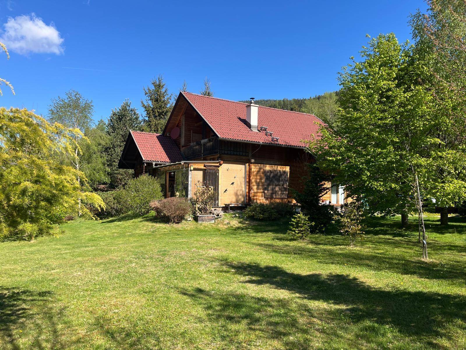 Weitläufiger Garten mit Bäumen und Blick auf das charmante Holzhaus und die Berge.