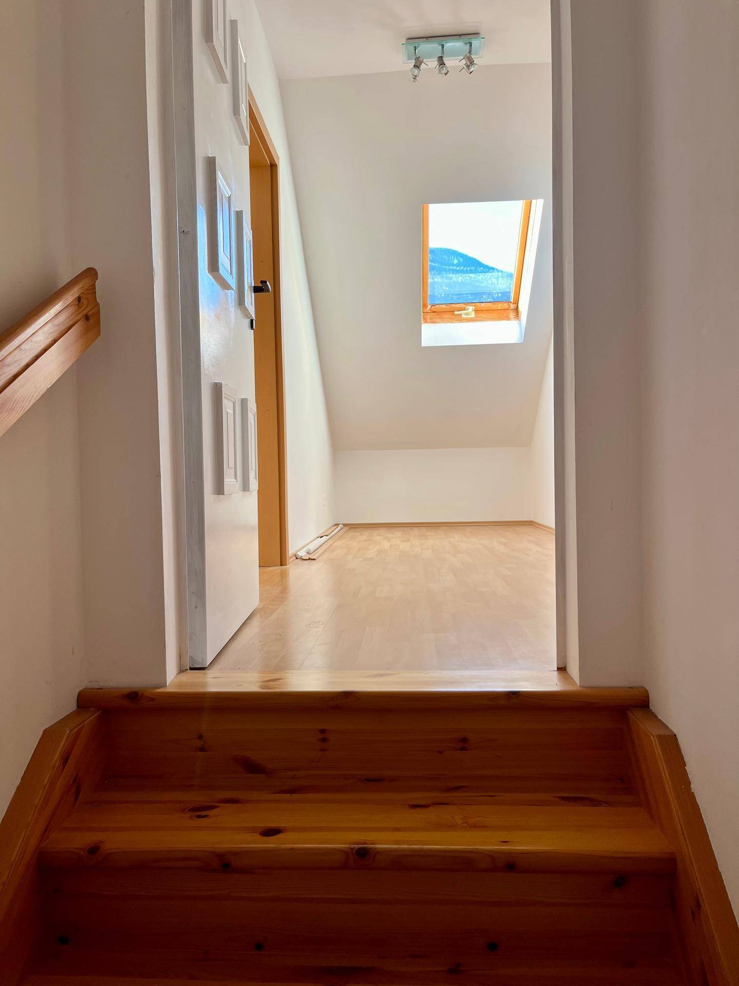 Holztreppe führt zum Dachgeschoss mit Dachfenster und hellem Holzboden.