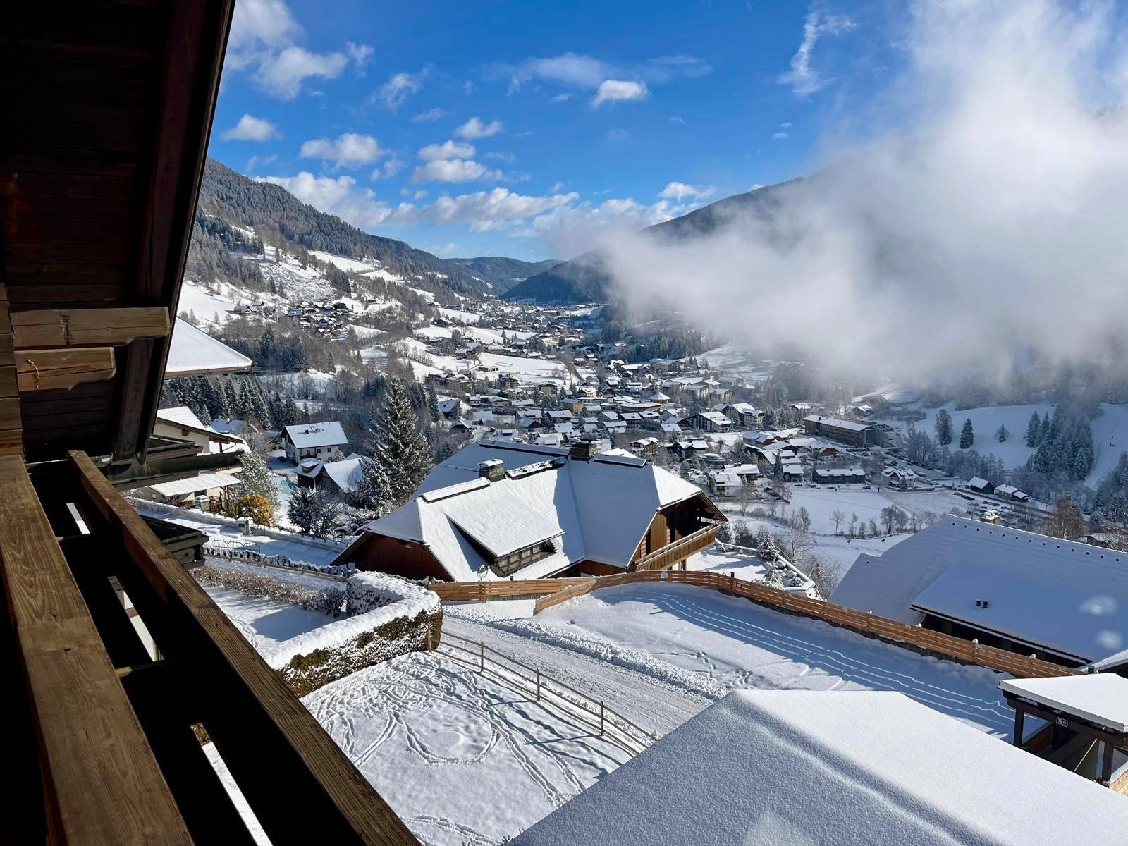 Panoramablick vom Balkon auf die verschneite Berglandschaft und das darunter liegende Dorf.