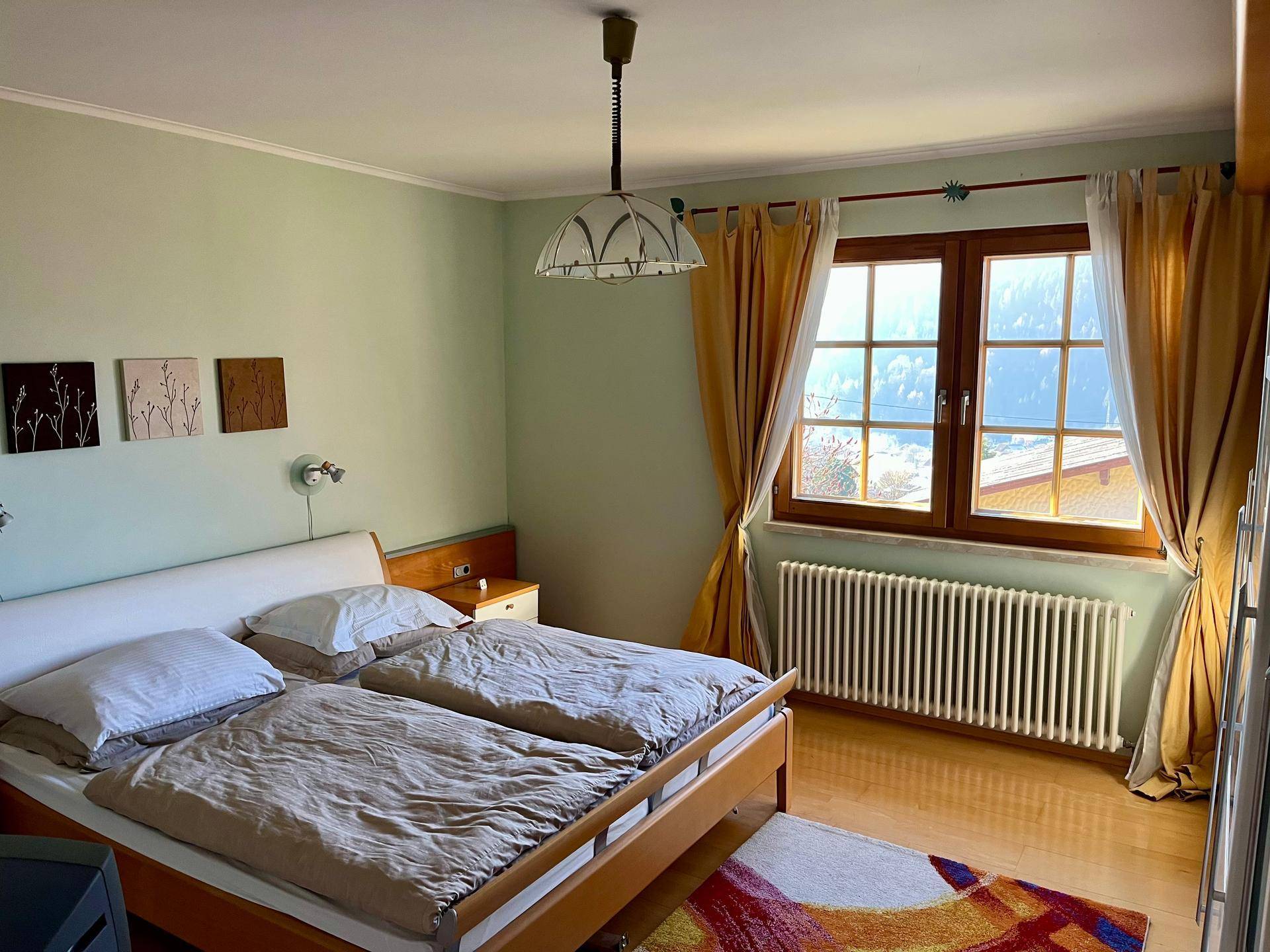 Gemütliches Schlafzimmer mit Doppelbett, Laminatboden und Blick auf die Berge.