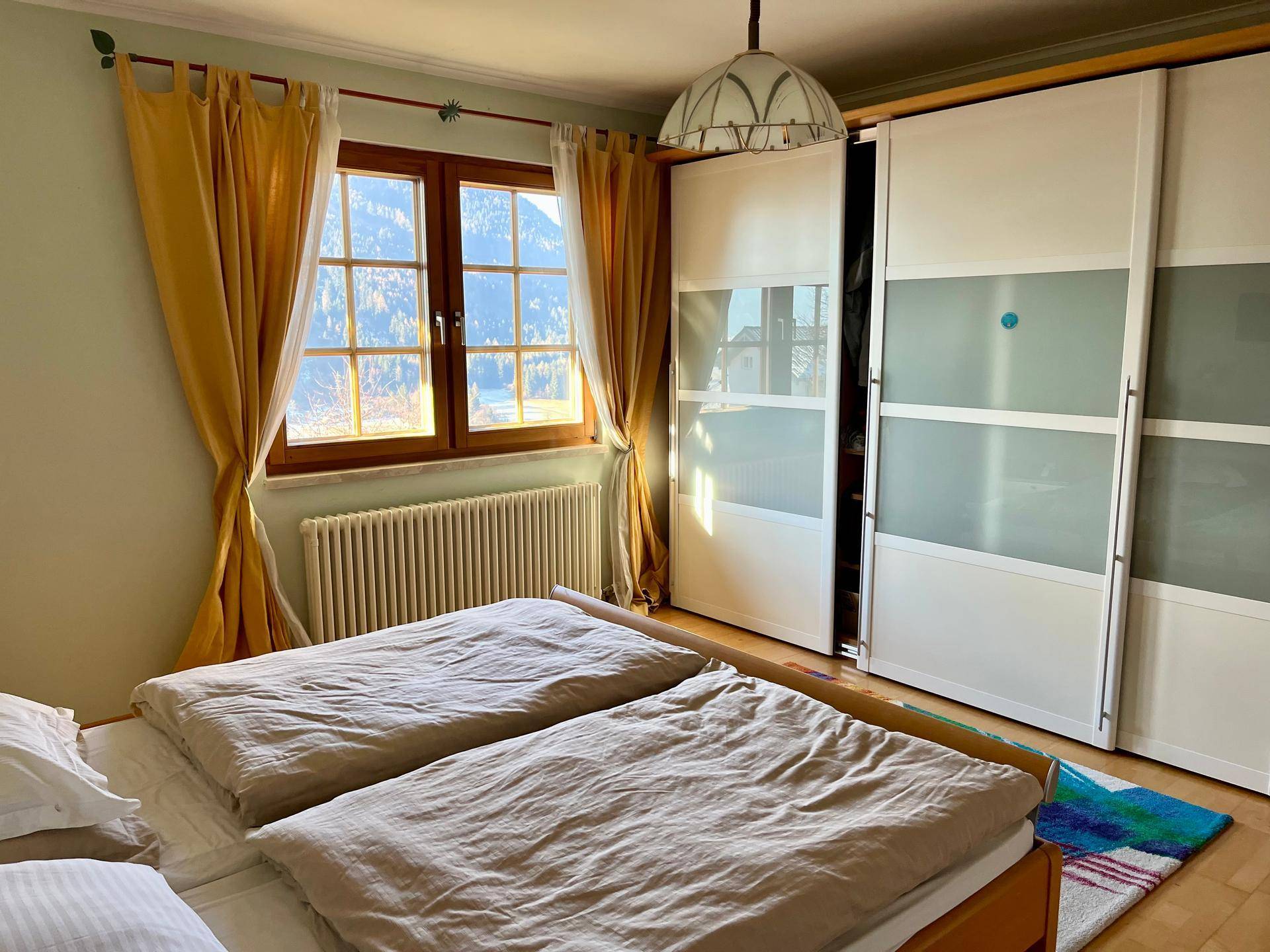 Schlafzimmer mit Schiebetürenschrank, Doppelbett und Fenster mit Bergblick.