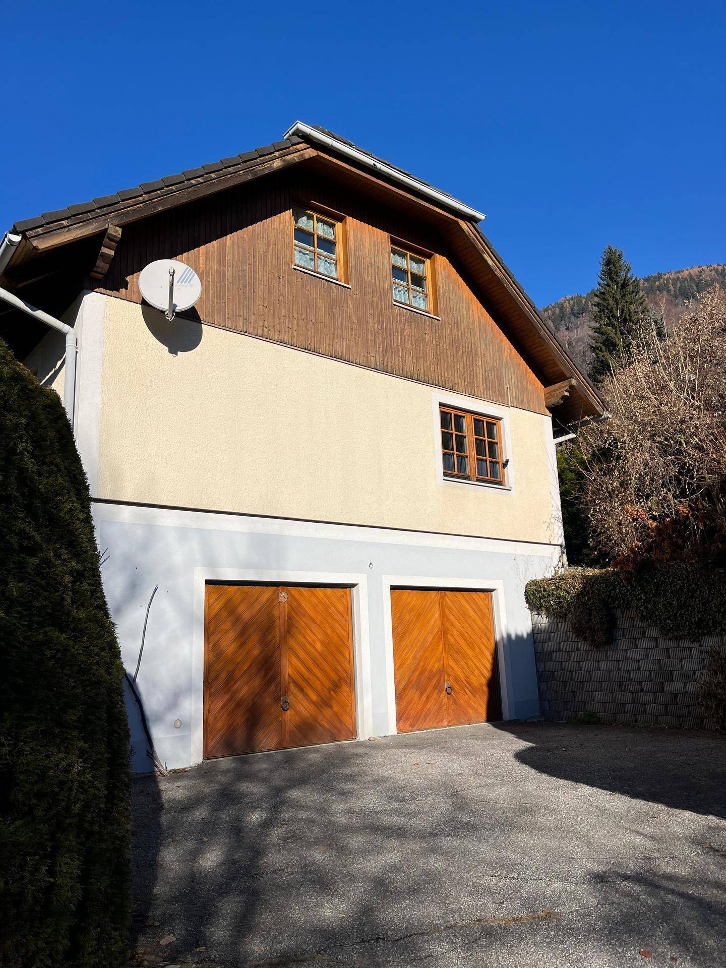 Seitenansicht des Hauses mit zwei Holzgaragentoren und einer Fassade in hellen Farbtönen.