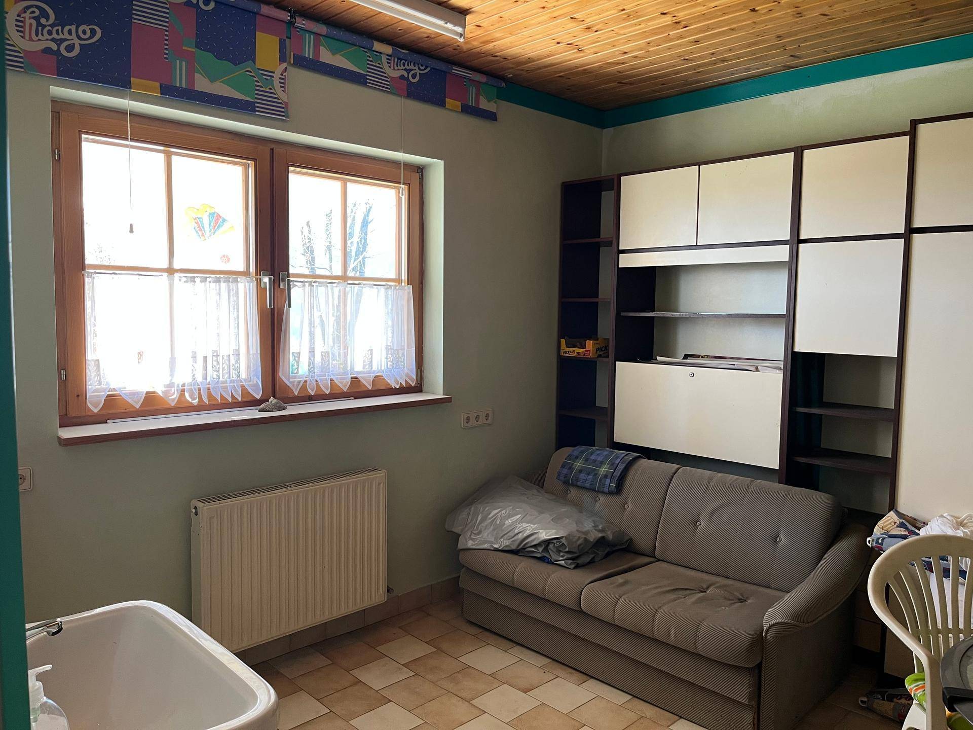 Praktischer Hauswirtschaftsraum mit Waschbecken, Sofa und Stauraum, ausgestattet mit Fliesenboden und Holzdecke.