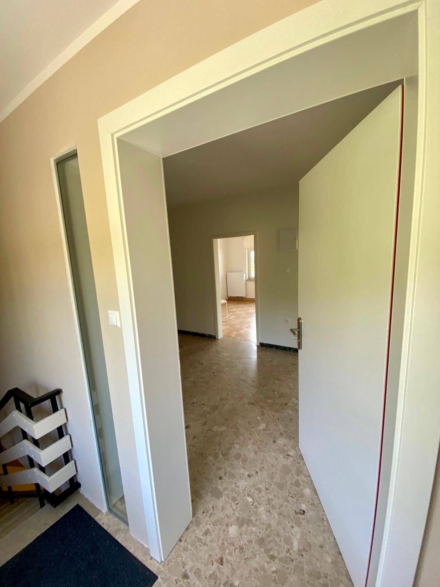 Eingangsbereich mit Fliesenboden und offener Tür, die den Blick in weitere Räume freigibt.