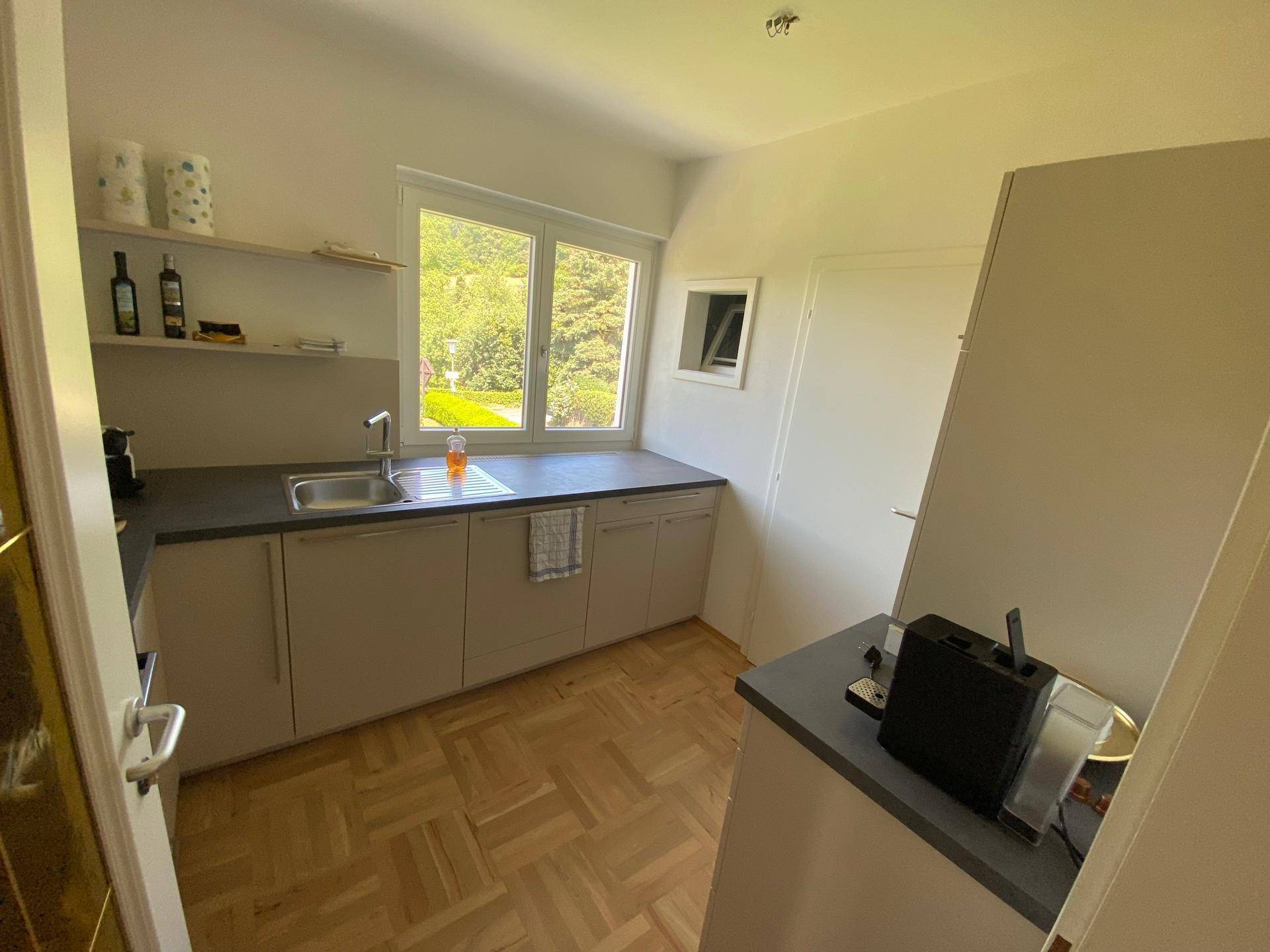 Helle Küche mit Holzparkettboden, modernen Unterschränken und Fenster mit Blick in den Garten.