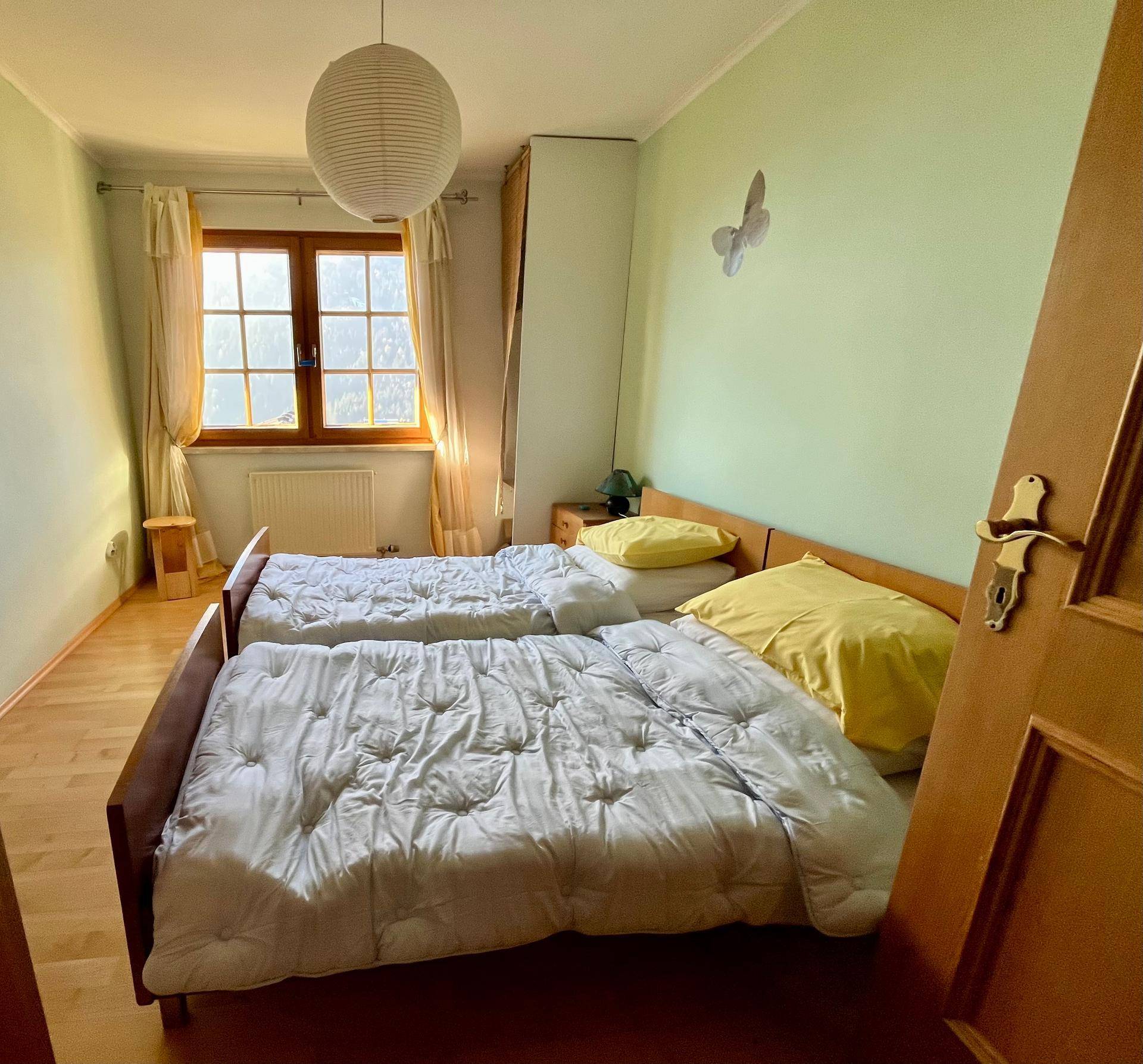 Schlafzimmer mit zwei Einzelbetten, hellem Laminatboden und Fenster mit viel Tageslicht.