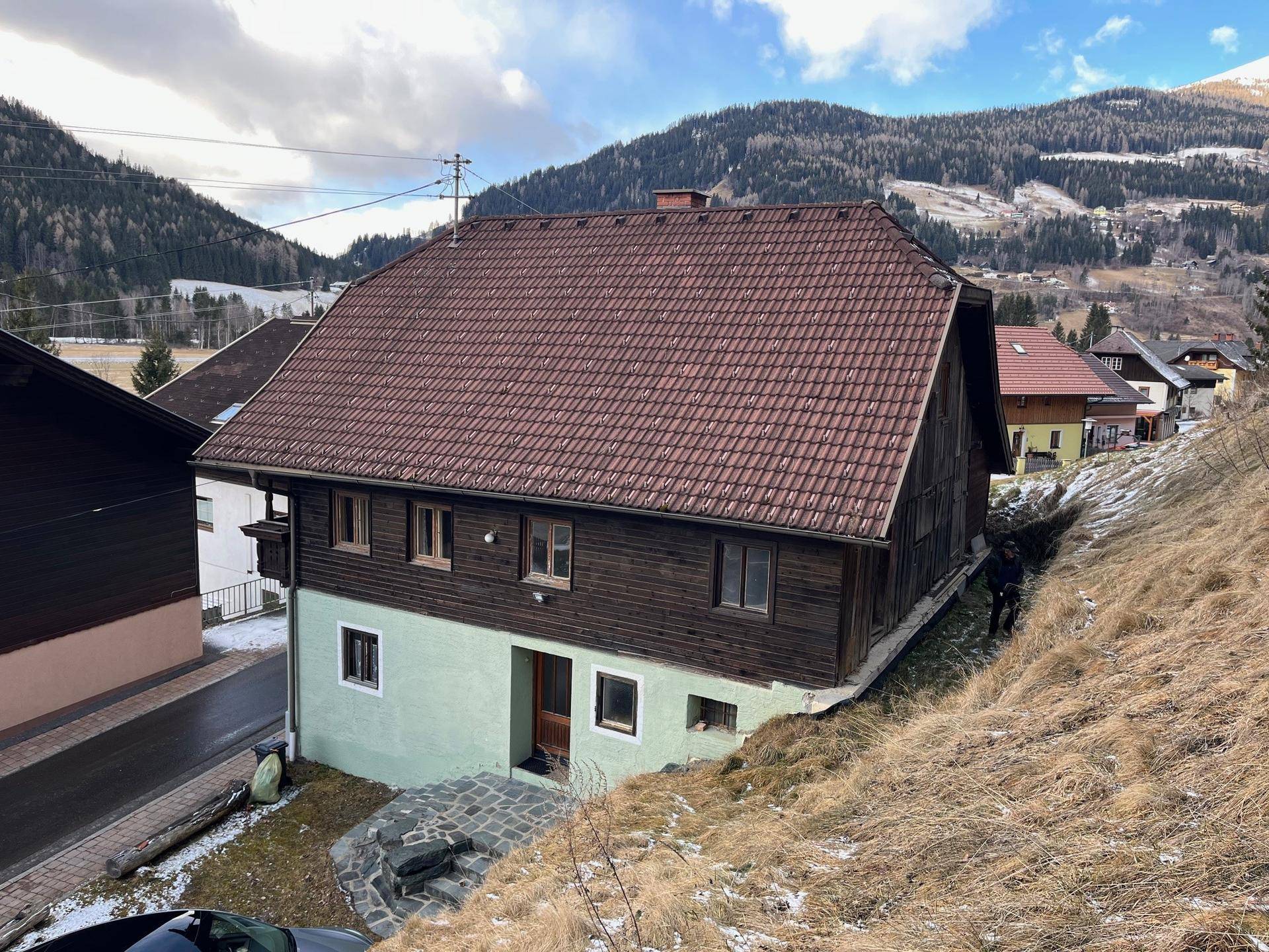 Traditionelles Haus in den Bergen mit Holzbalkonen und Ziegeldach, umgeben von winterlicher Landschaft.