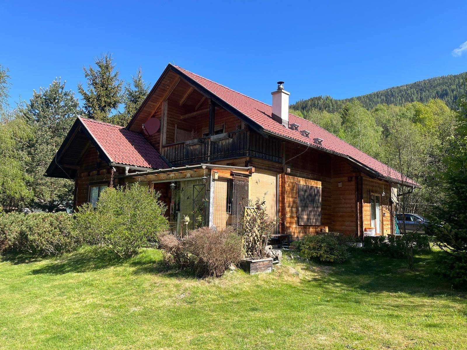 Rustikales Holzhaus mit traditionellem roten Dach, eingebettet in eine grüne Hügellandschaft.