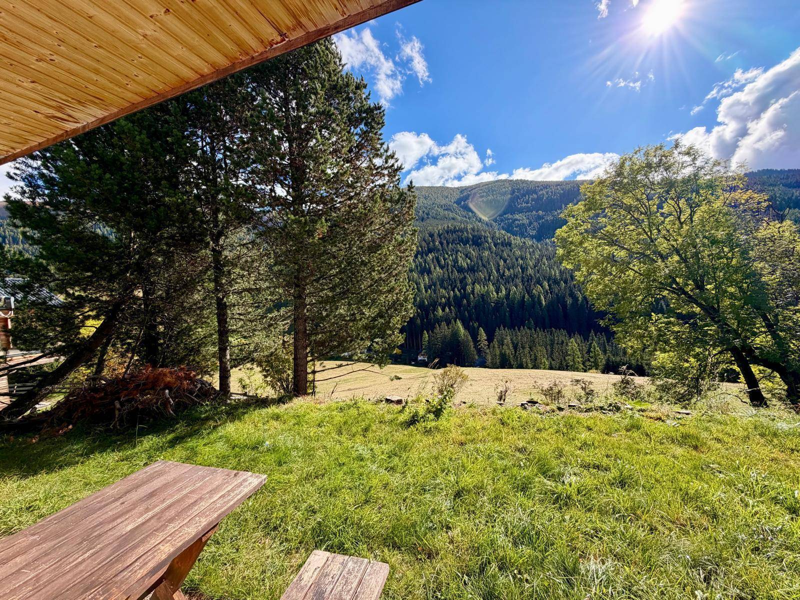 Gemütlicher Sitzbereich im Garten mit Holztisch und weitem Blick auf die sonnige Berglandschaft.